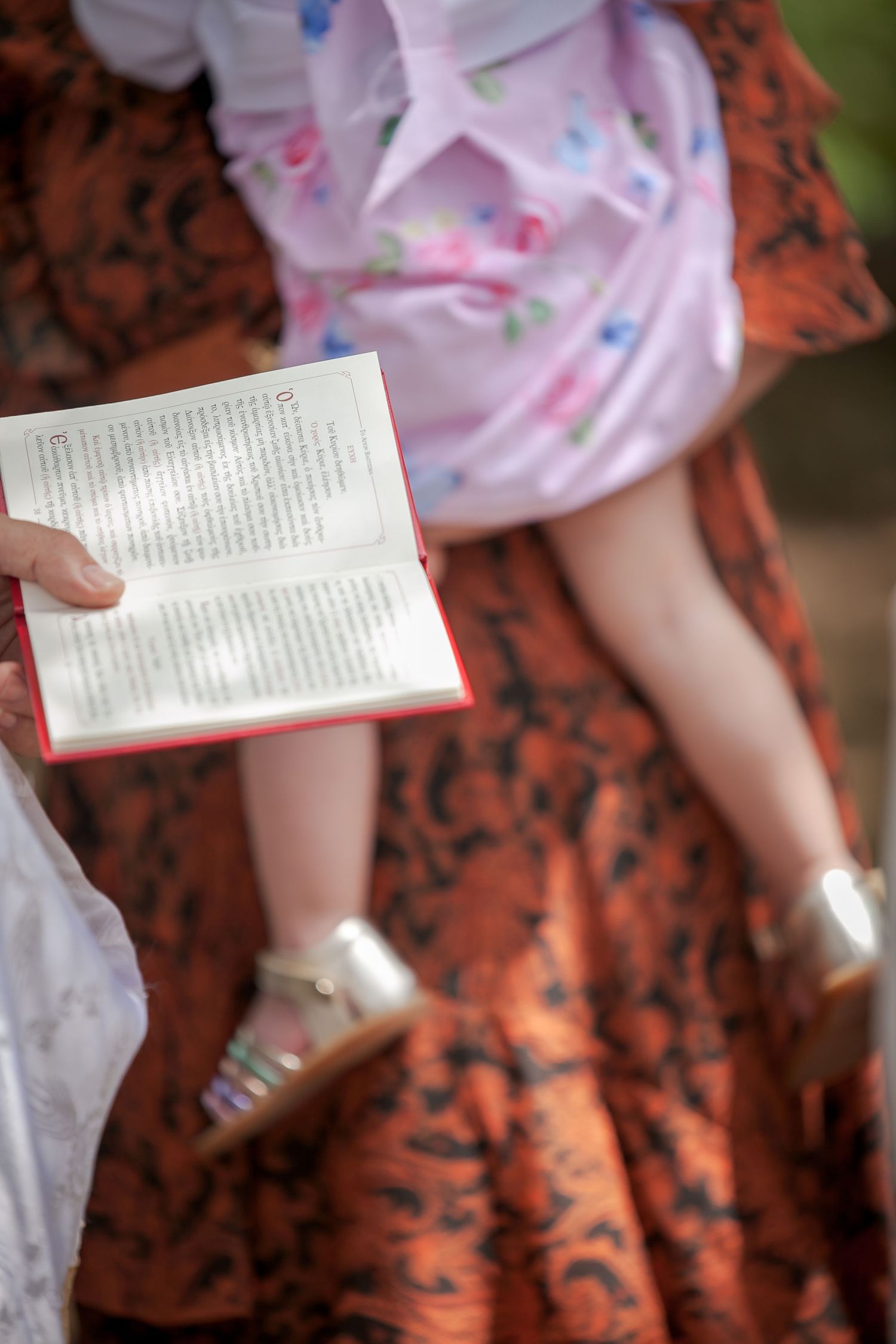 Woman in floral dress reading a book outdoors.
