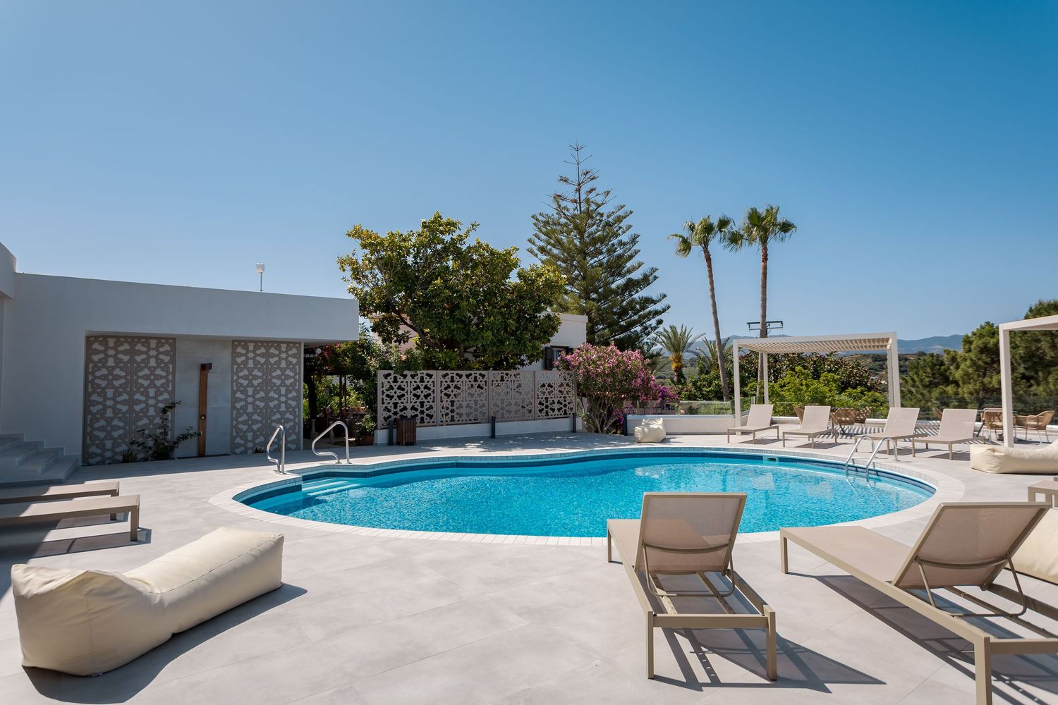 Panoramic view of a modern resort swimming pool with sun loungers overlooking the bright blue ocean on a sunny day.