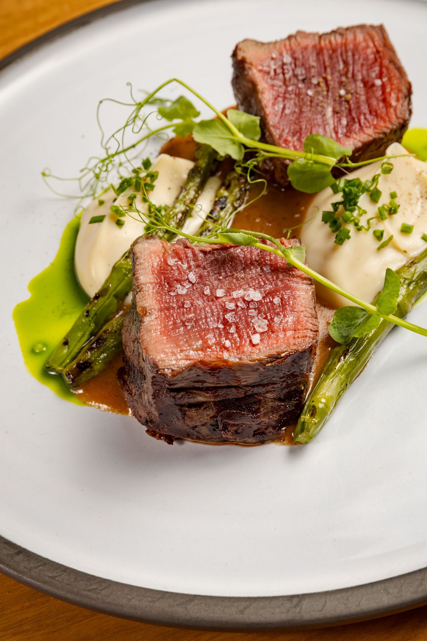 Perfectly cooked medium-rare beef tenderloin steak plated with microgreens and sauce on a white ceramic dish.