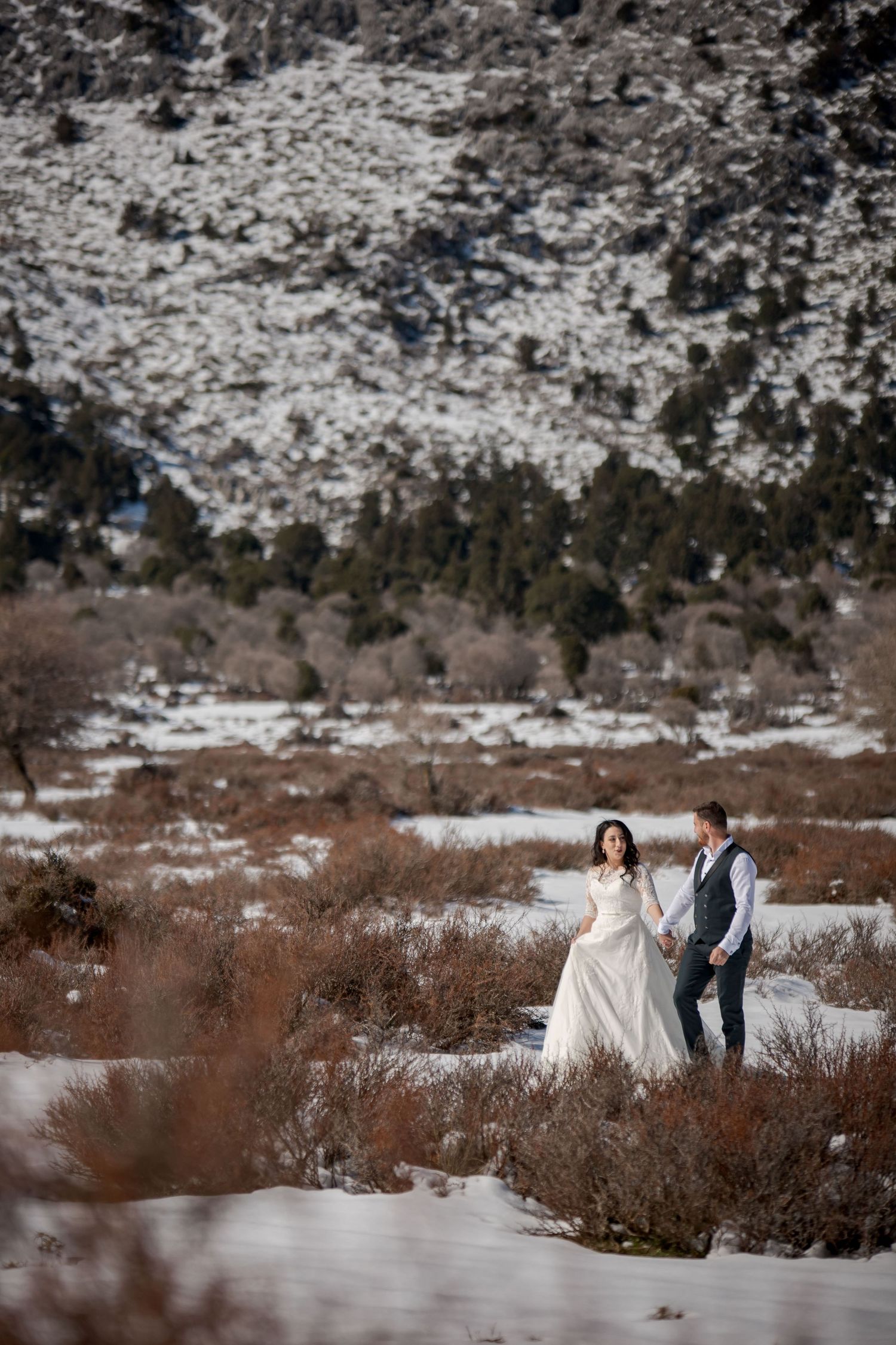Wedding couple poses in snowy mountain landscape with dramatic winter scenery.