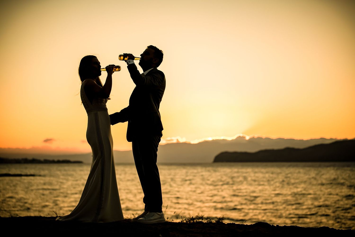 Romantic silhouettes of a couple posing against a sunset at the beach with orange sky in the background.