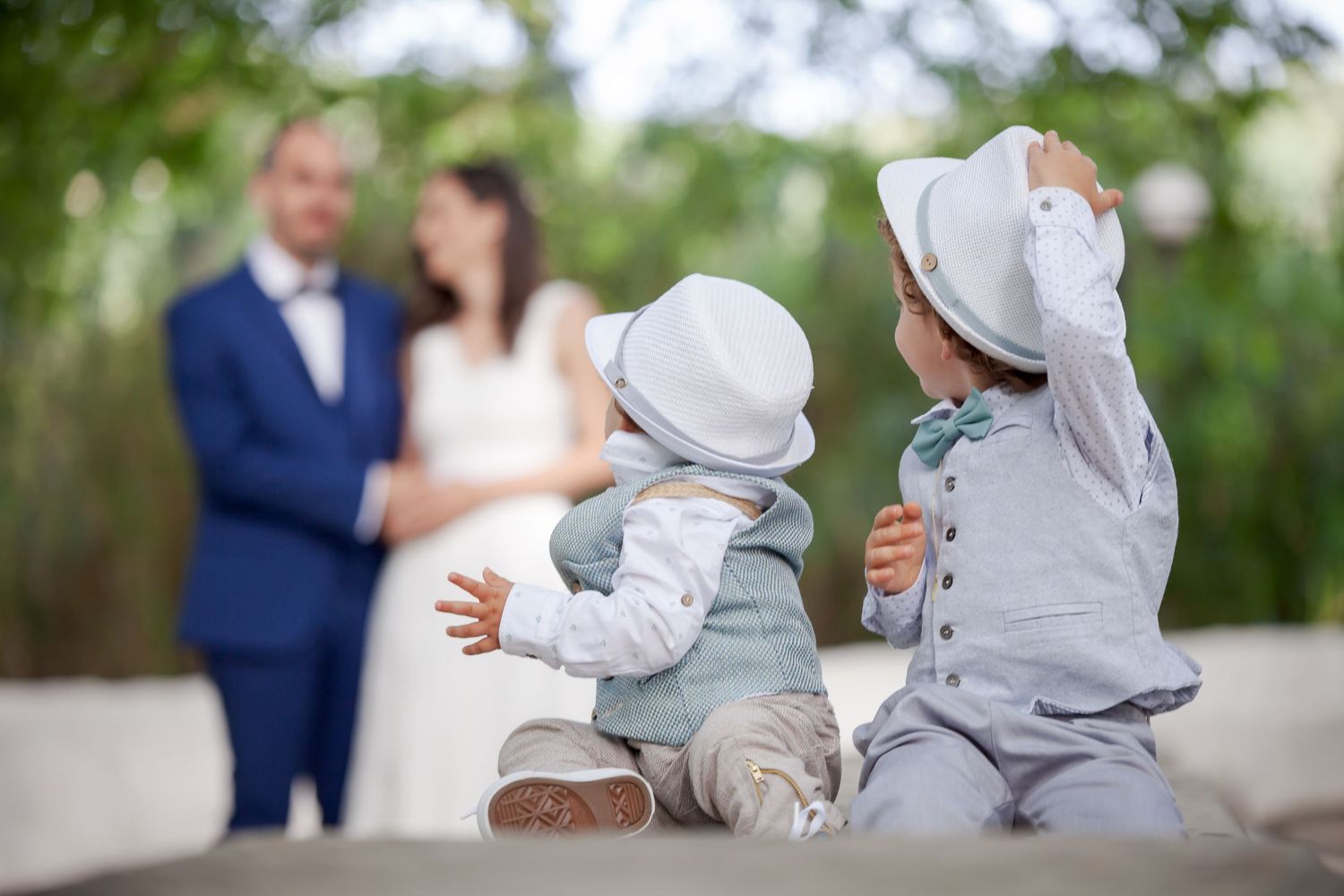 Small baby in grey outfit sits on ground against nature backdrop during outdoor photography session.