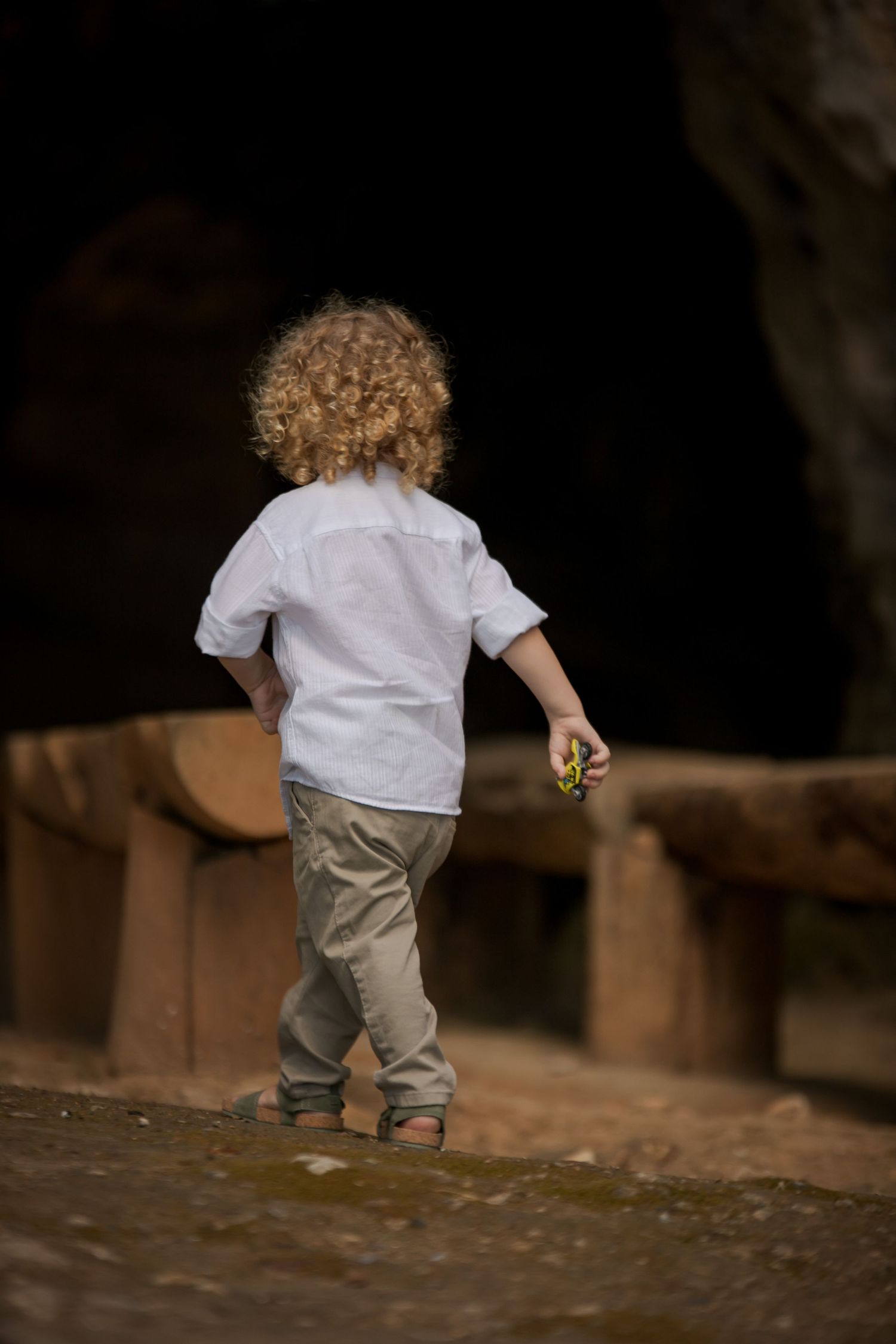 Small child in white shirt and gray pants walking on stone surface.