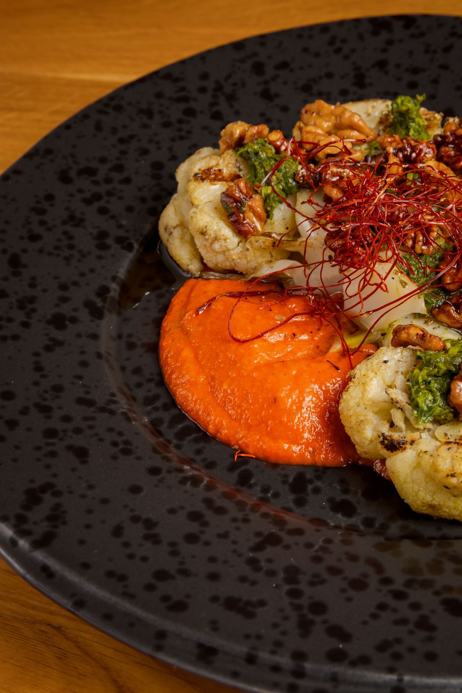 Orange puree serves as a vibrant base for perfectly grilled seafood and delicate garnishes on a matte black plate.