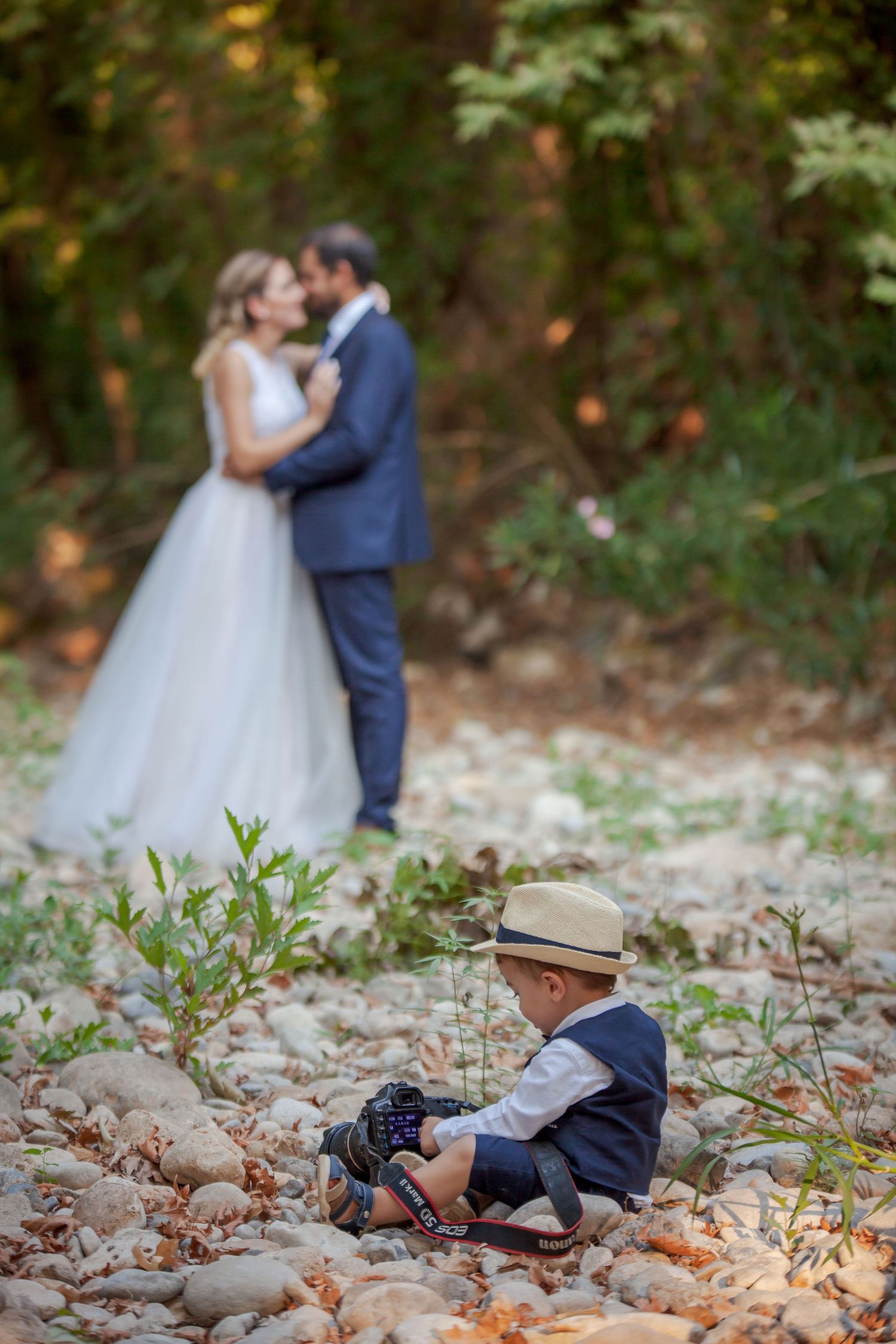 Wedding couple shares intimate moment in forest while small child plays in fallen leaves.