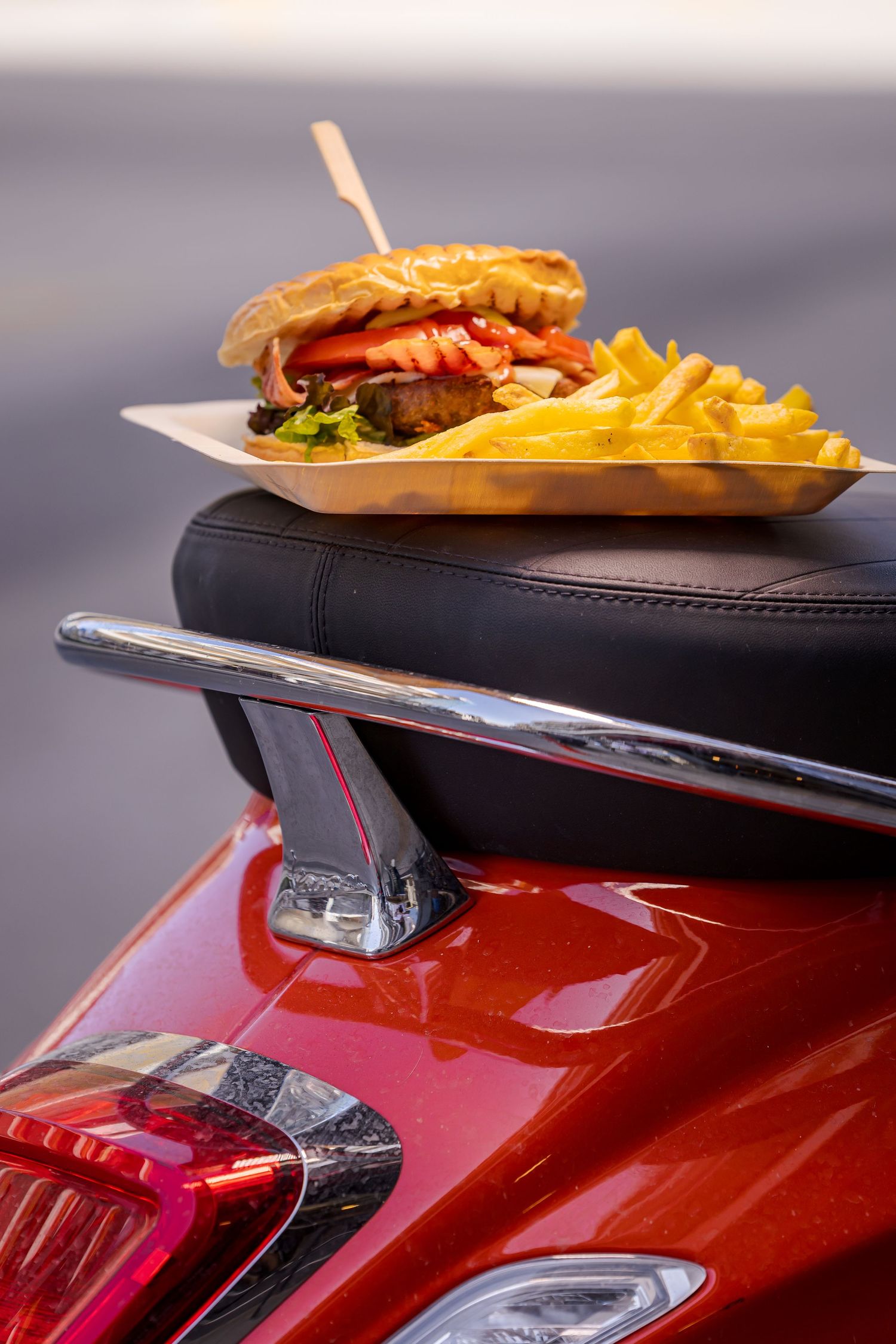 A fast food meal with burger and fries served on the rear spoiler of a shiny red sports car.