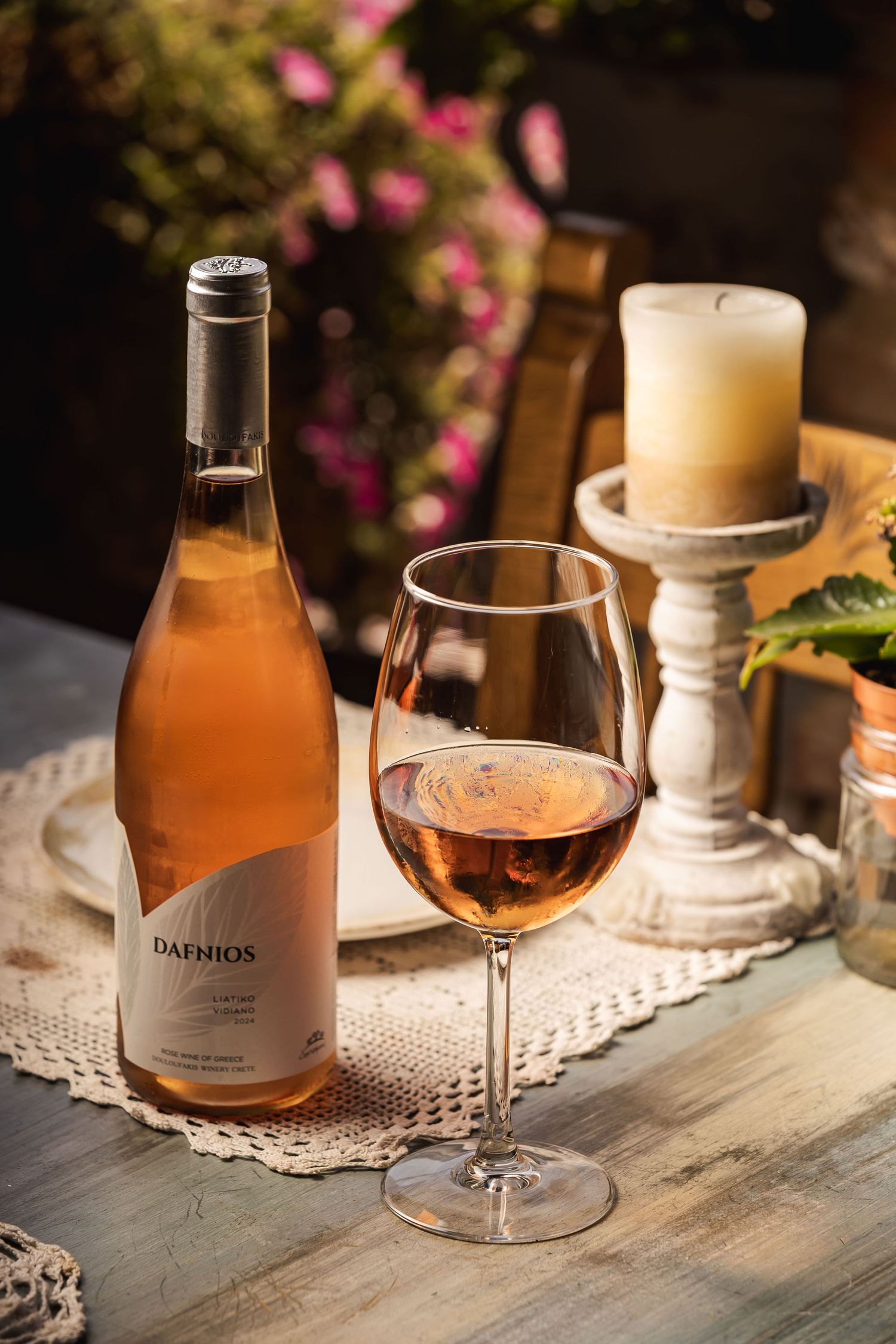 A romantic table setting features glasses of rosé wine with soft pink flowers and lace doilies in warm lighting.