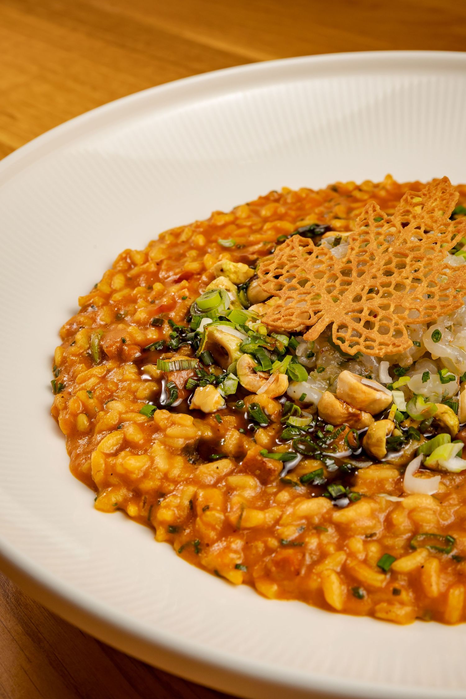 Creamy orange risotto garnished with fresh herbs and a delicate wafer crisp on a white plate.