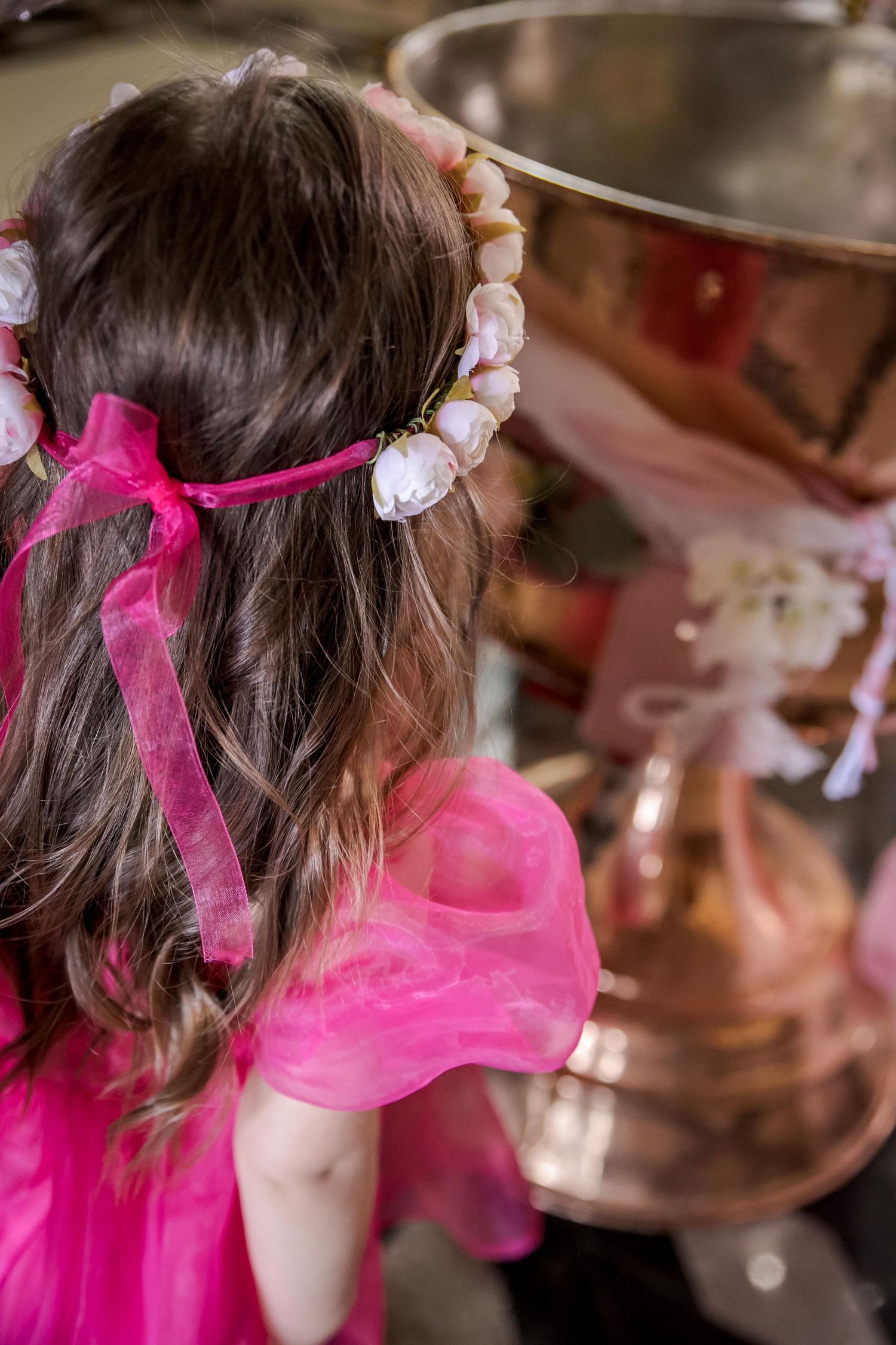 A pink ribbon and floral headpiece adorns brown hair at a formal event.