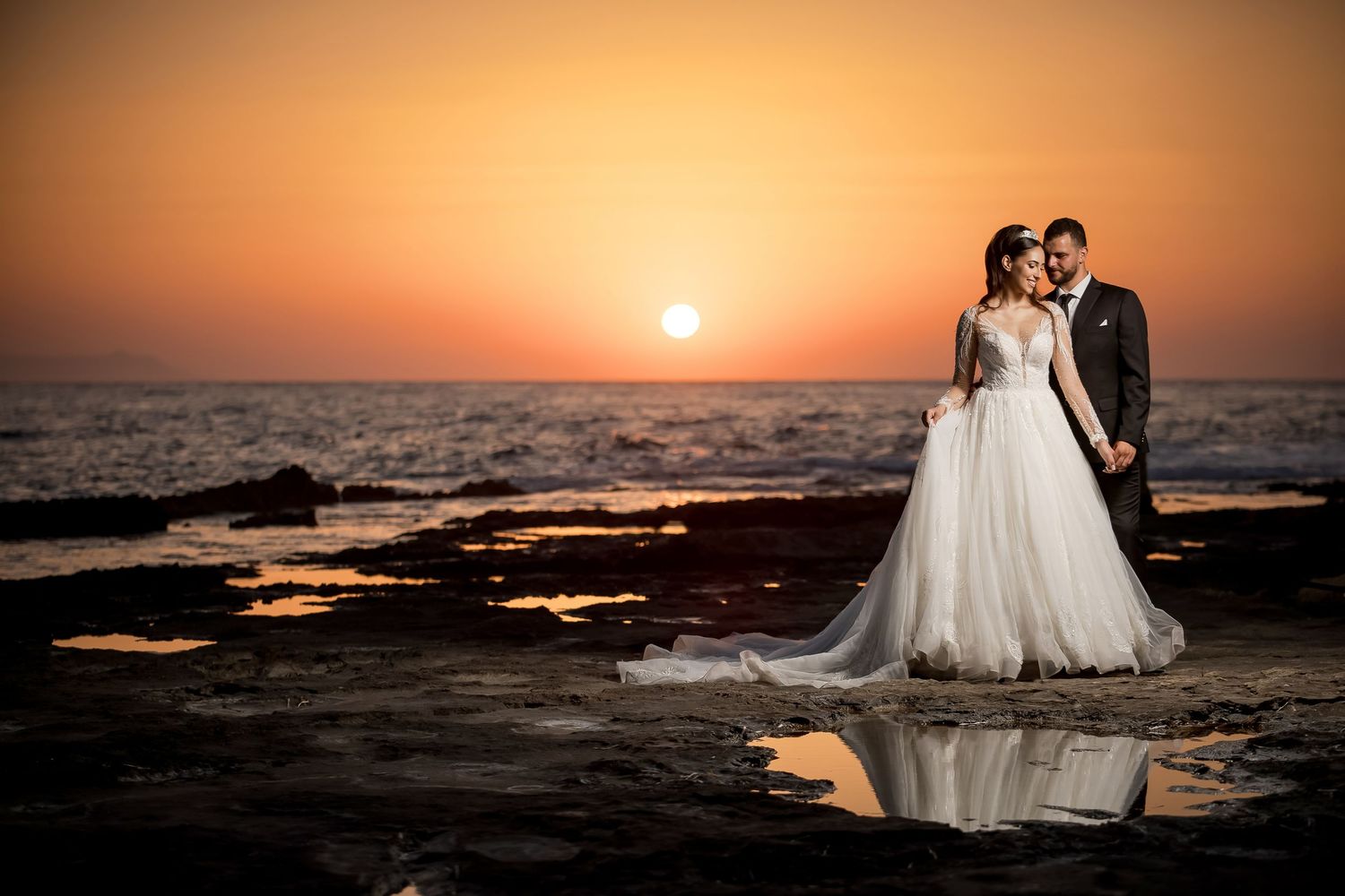 Golden sunset wedding photos by ocean with silhouetted couple against orange sky.