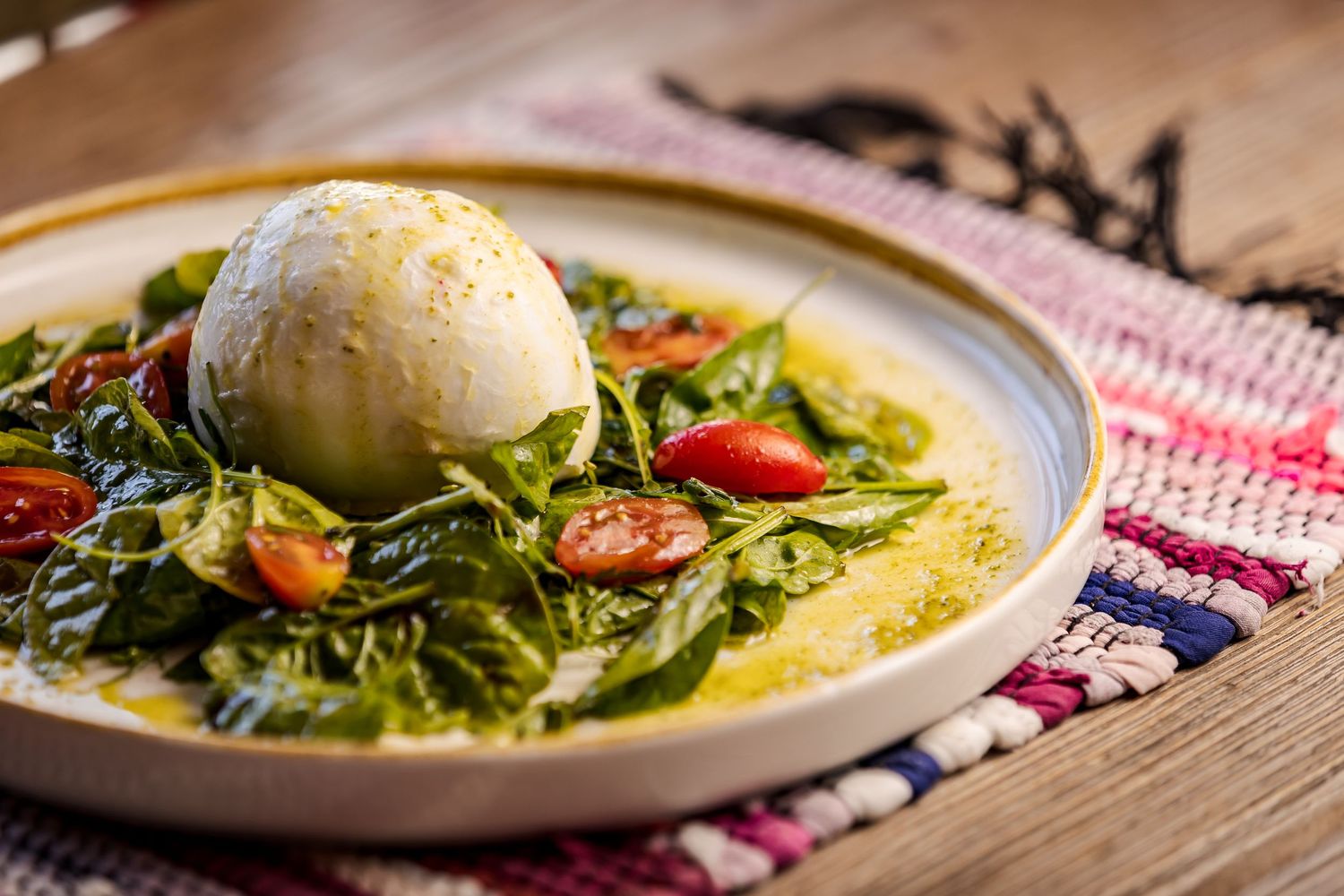 Six plates of creamy yellow burrata cheese served with fresh arugula, tomatoes and olive oil on rustic tableware.