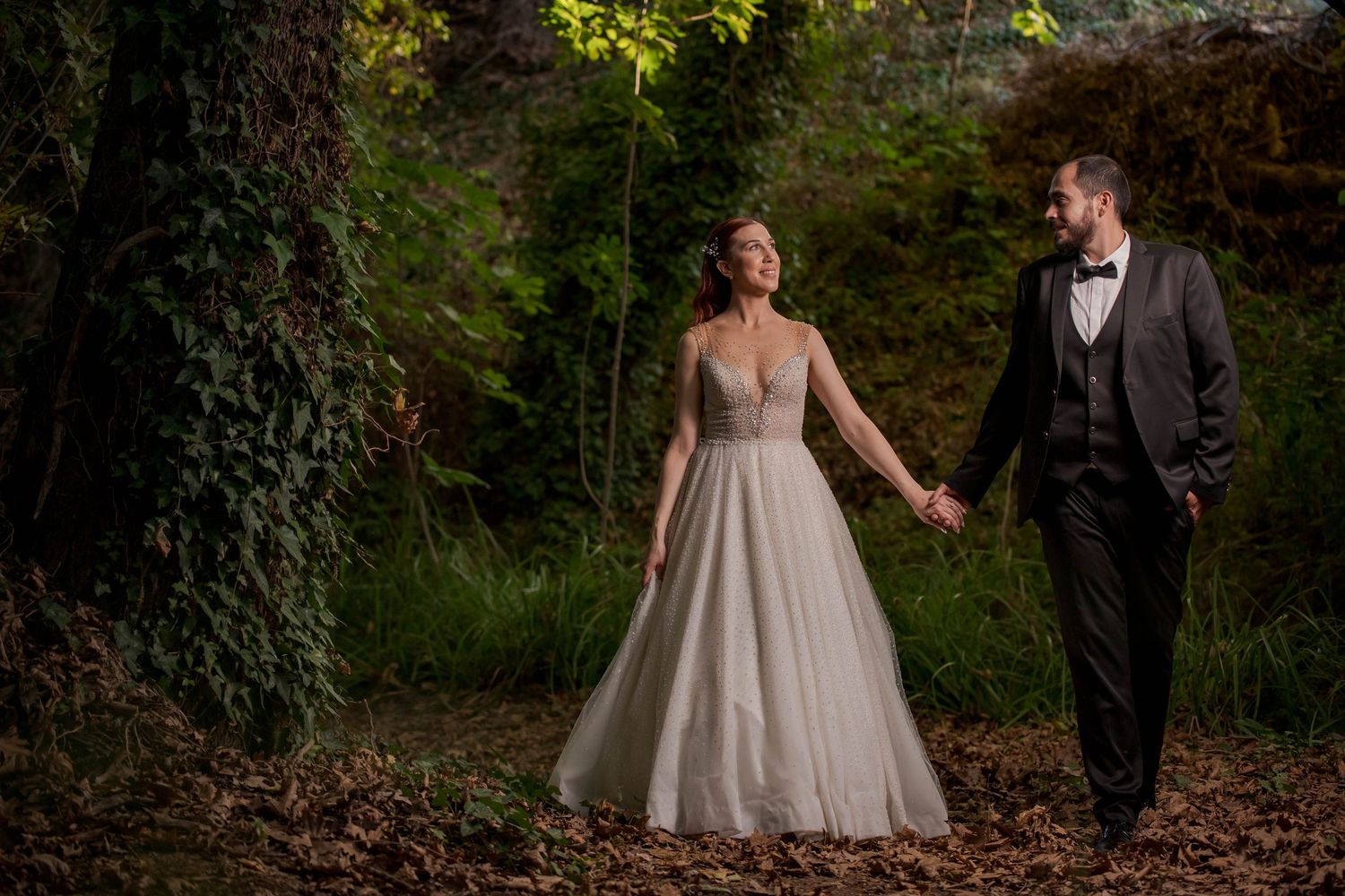 Couple walks through lush garden pathway during autumn wedding photoshoot.