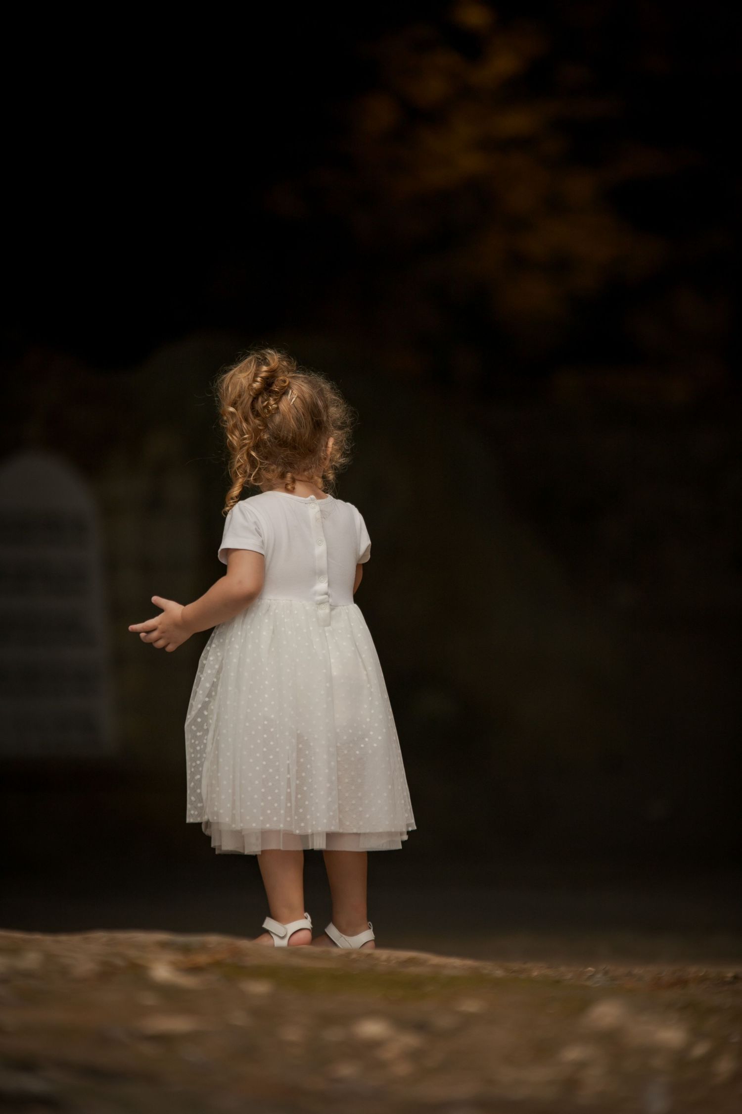Small child in white dress exploring outdoor setting.