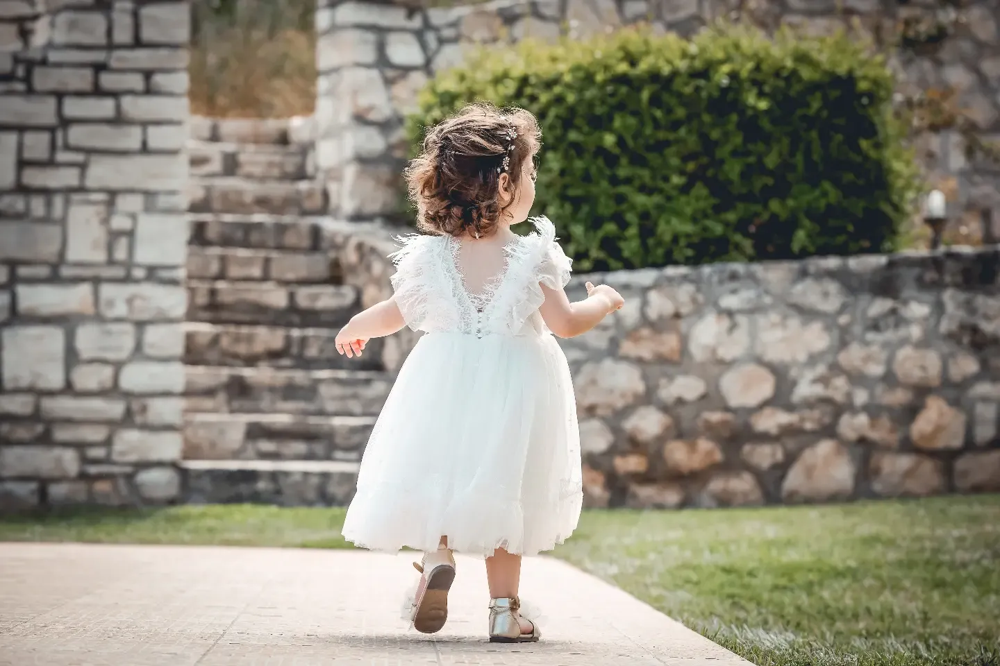 Children in formal wear walk along a stone wall pathway.