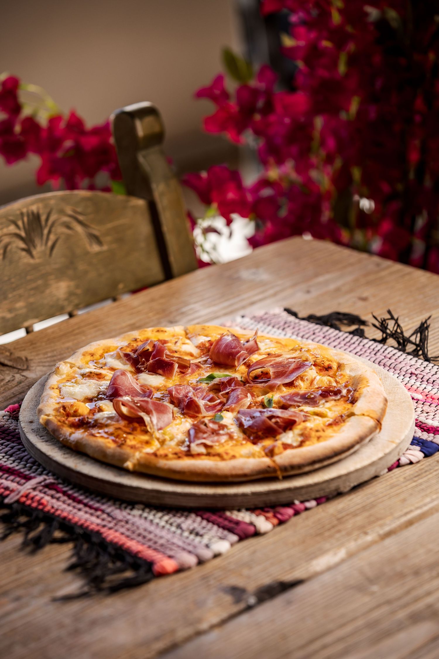 Delicious homemade pizza with meat toppings on a rustic wooden table decorated with pink flowers and a gingham cloth.