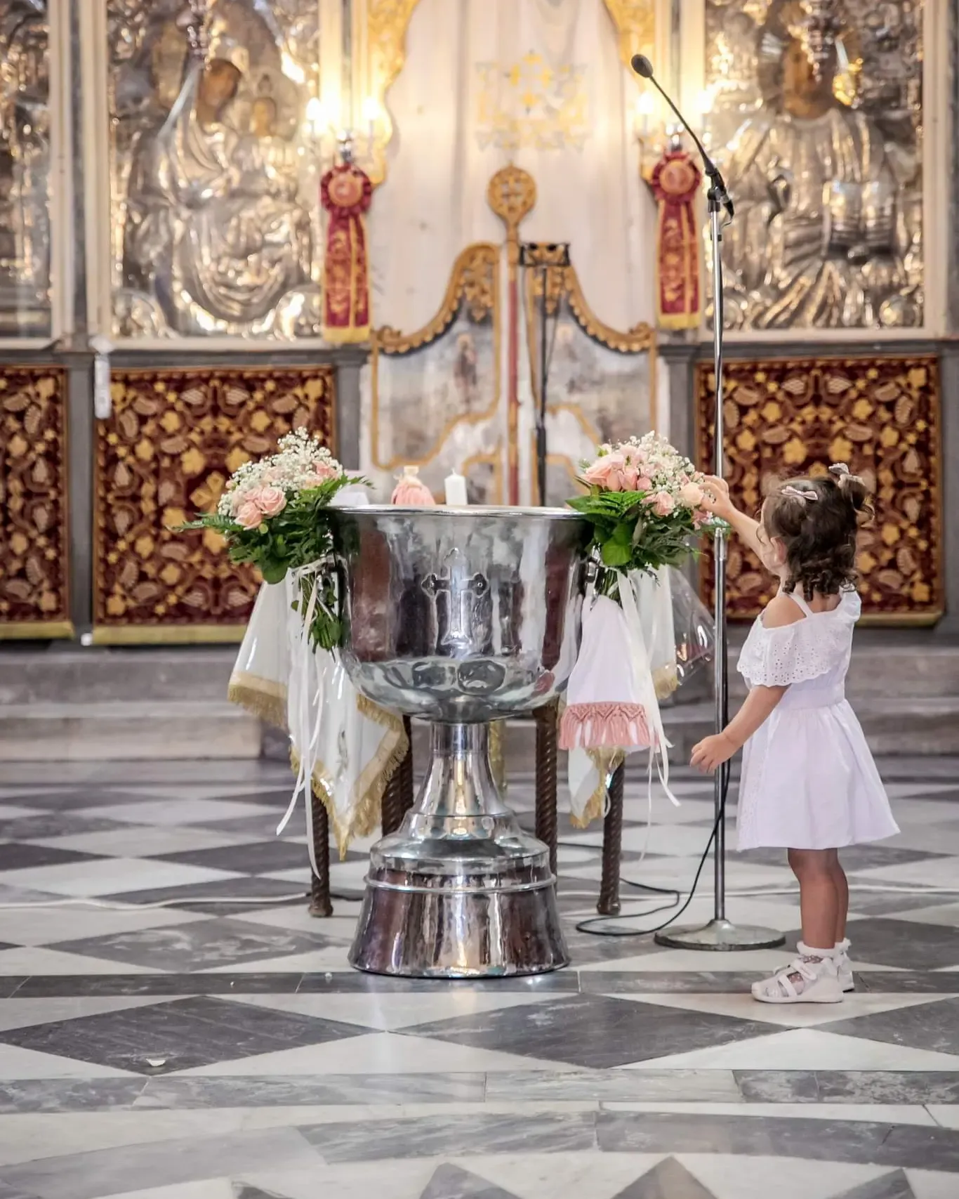 Young attendant in white dress walking through ornate baroque church interior with floral decorations.