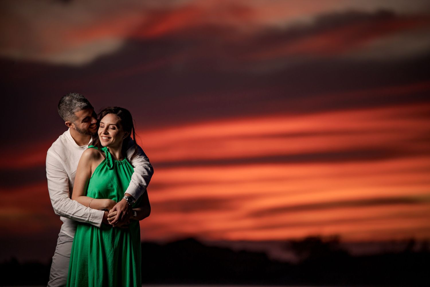 Couple embracing against vibrant red sunset sky.