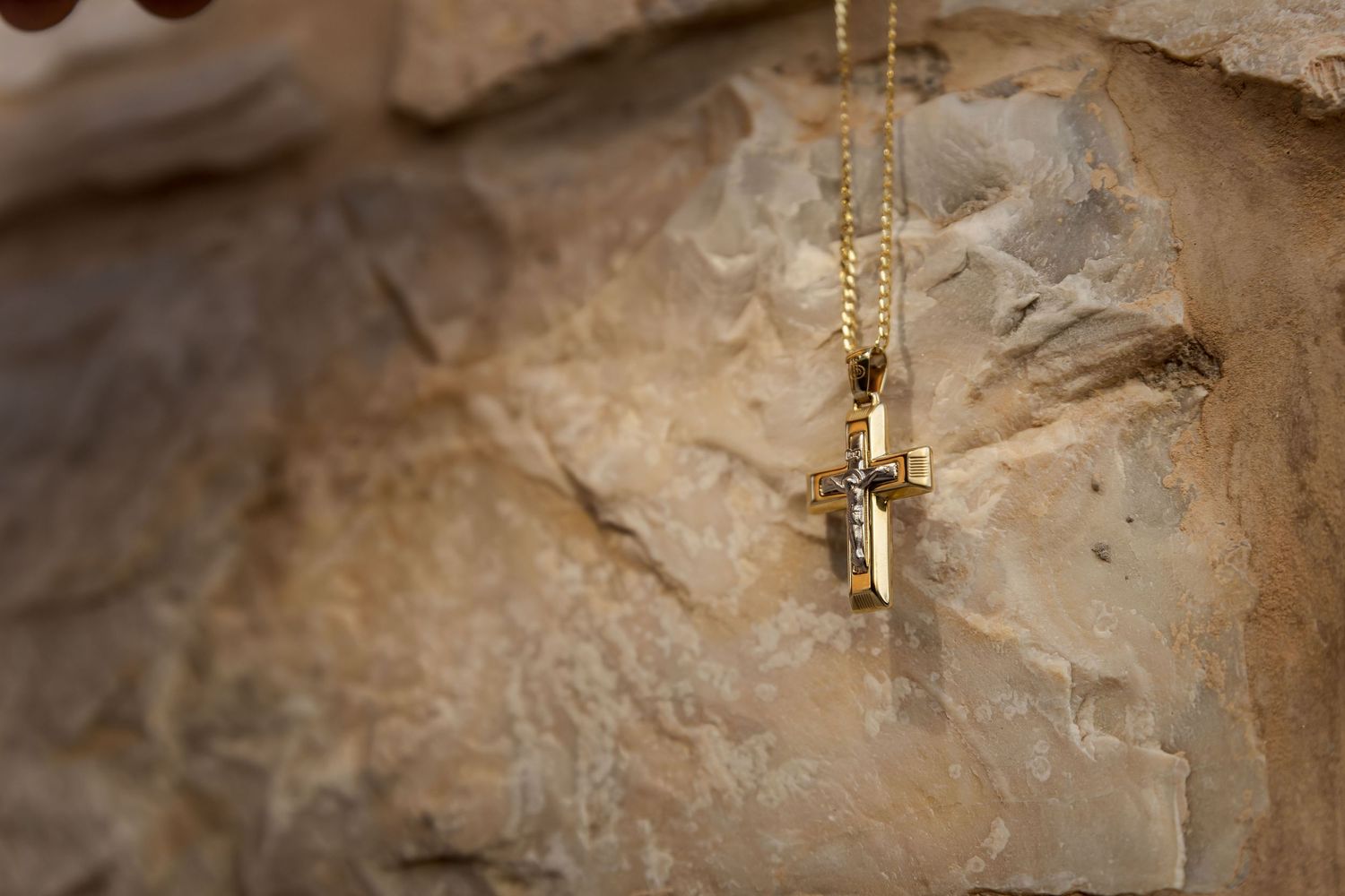 Gold necklace or pendant hanging against textured stone wall background.