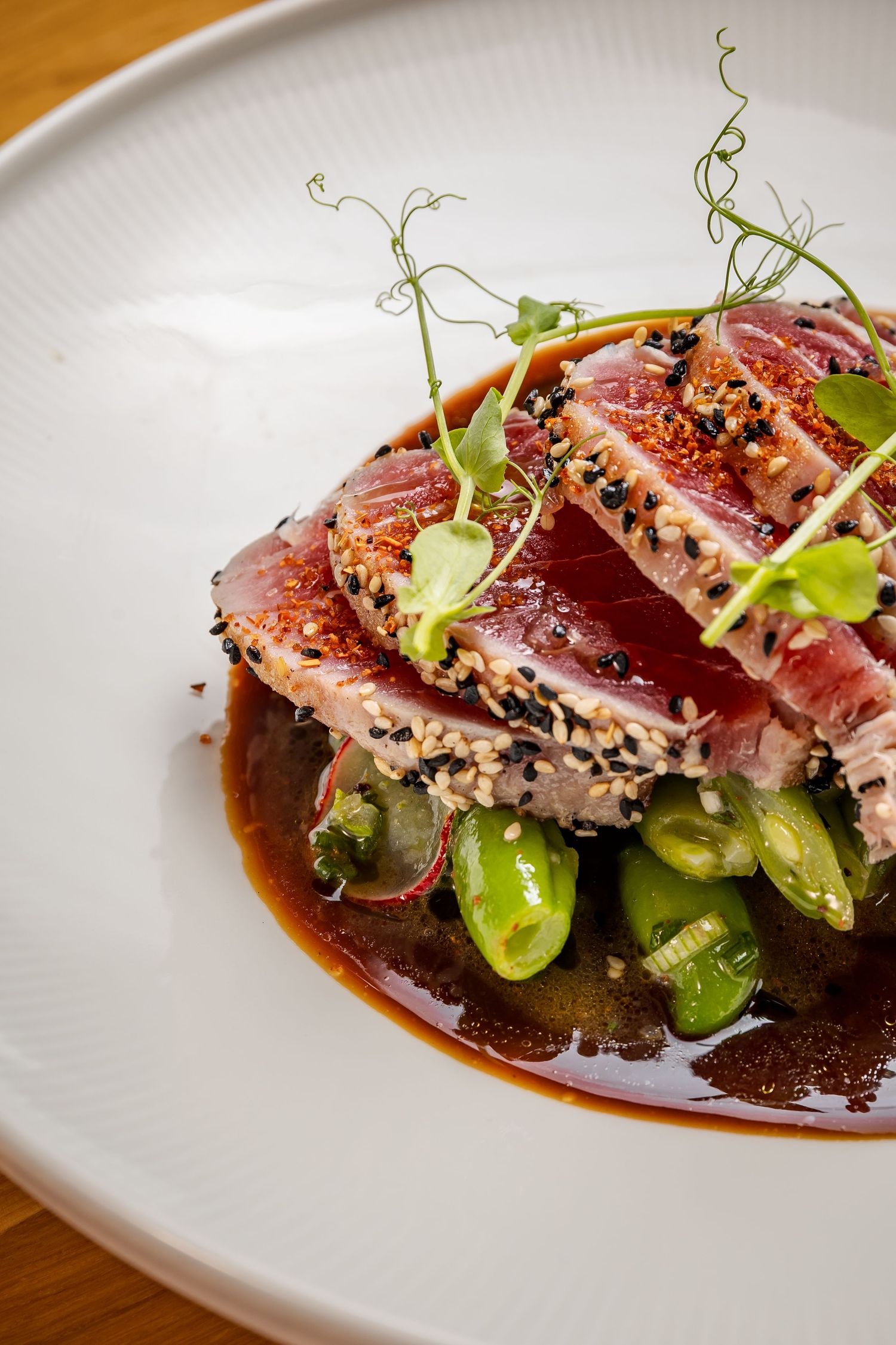 Seared tuna slices with microgreens and soy sauce artfully plated on a white ceramic dish in a fine dining presentation.