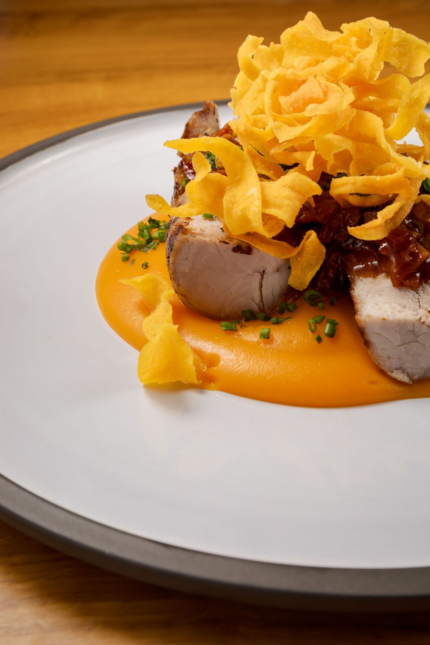 Elegantly plated dish featuring sliced meat with orange sauce and crispy garnish on a white plate.