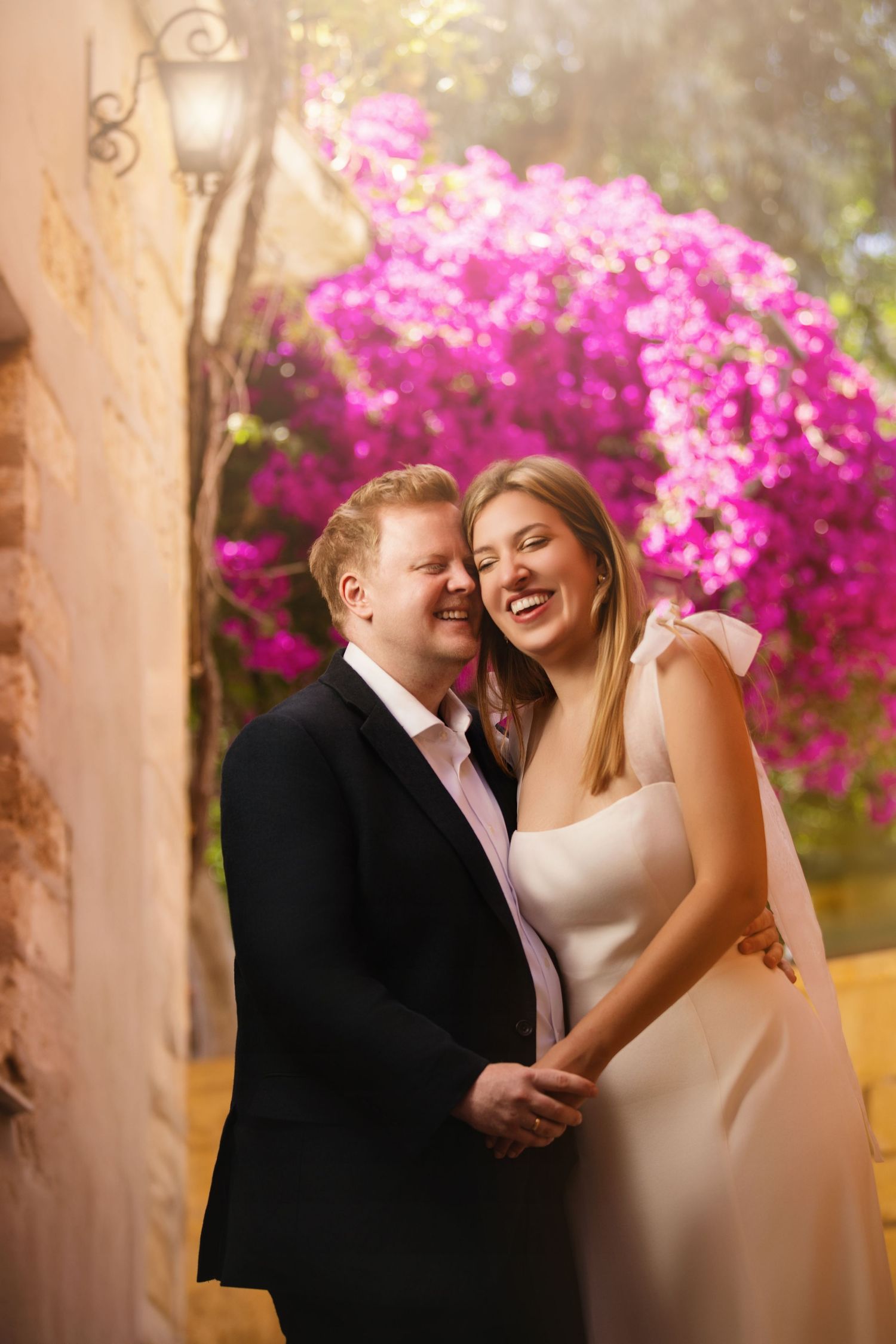 A joyous wedding couple laughing together against beautiful pink bougainvillea flowers.