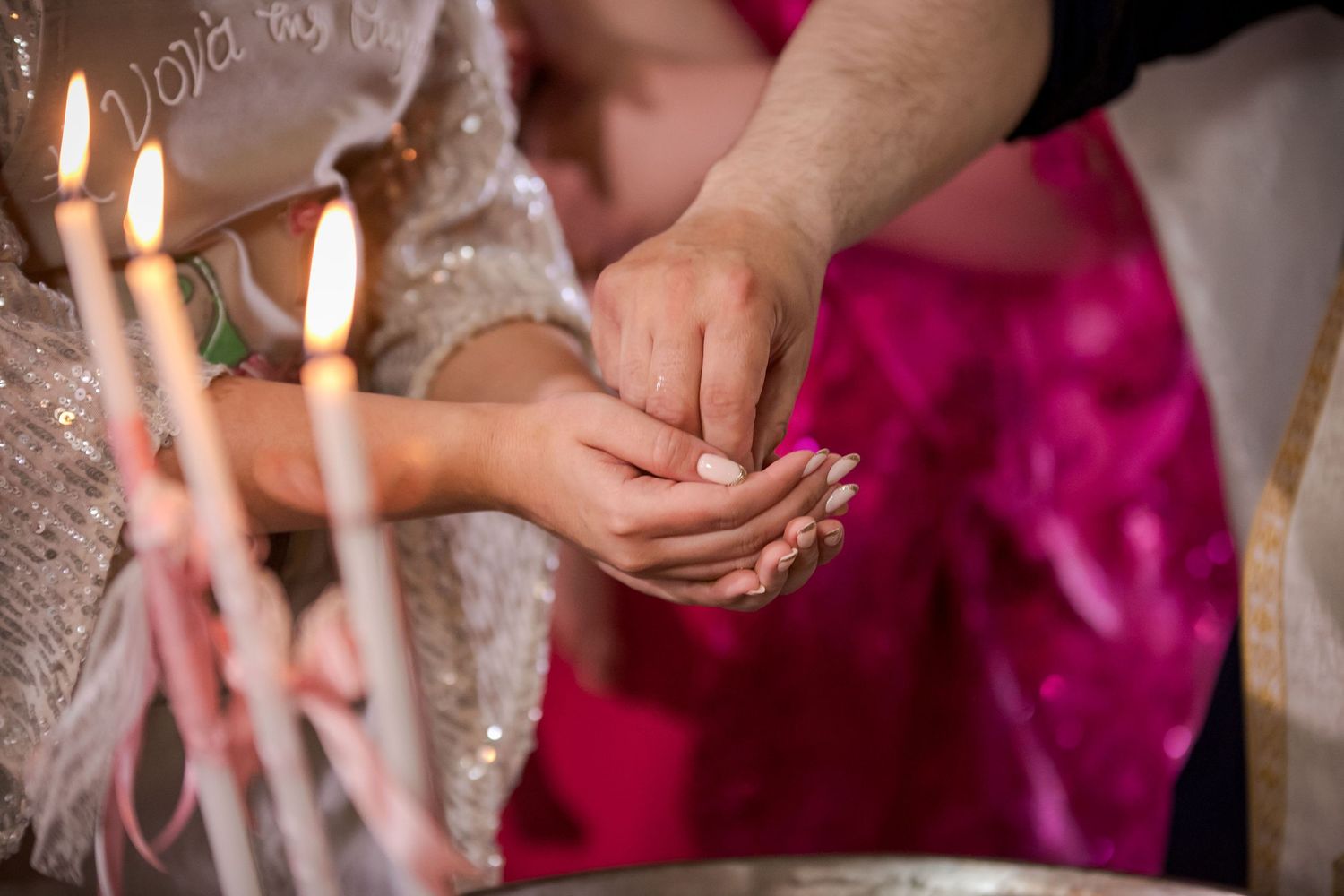 Hands holding candles against shimmering dress fabric and pink background.
