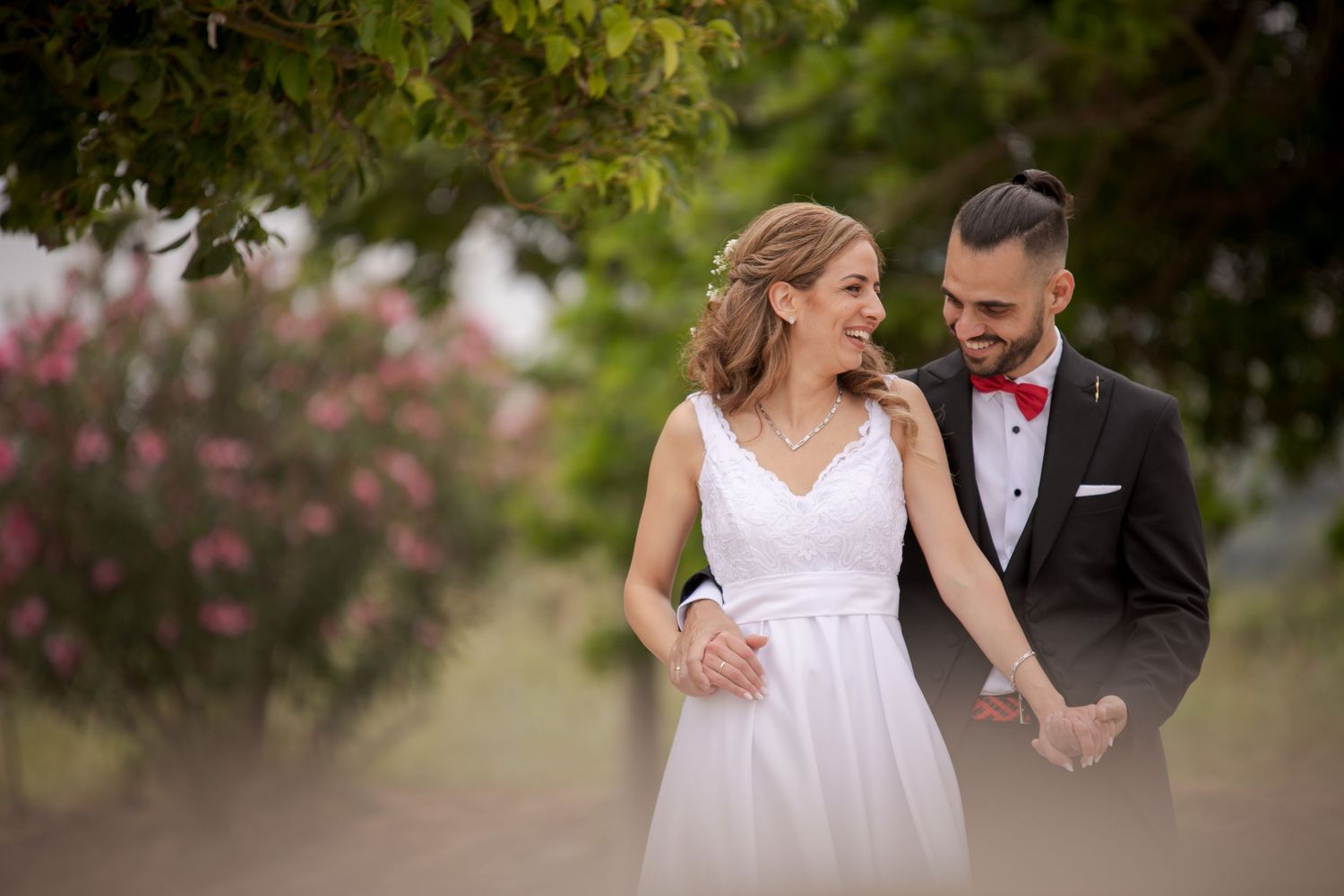 Wedding couple poses in garden setting with blooming flowers and natural greenery.