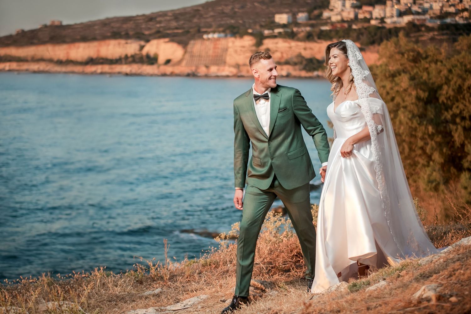 Wedding couple poses along coastal cliffs during golden hour photography session.