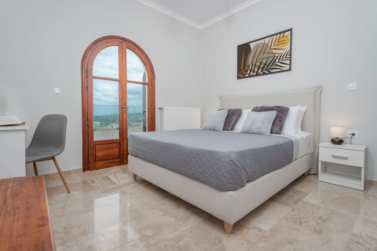 Bright and airy bedroom interior with grey bed linens, wooden flooring, and contemporary white furnishings.