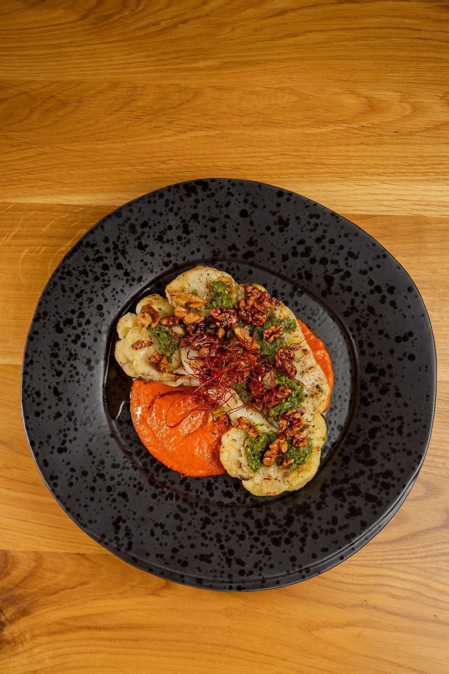 Black matte plate with tomato and pasta dish garnished with fresh herbs and spices served on wooden table.