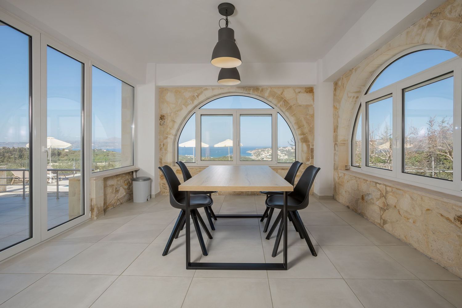 Modern dining room with large arched window and panoramic views, featuring black furniture and natural light.