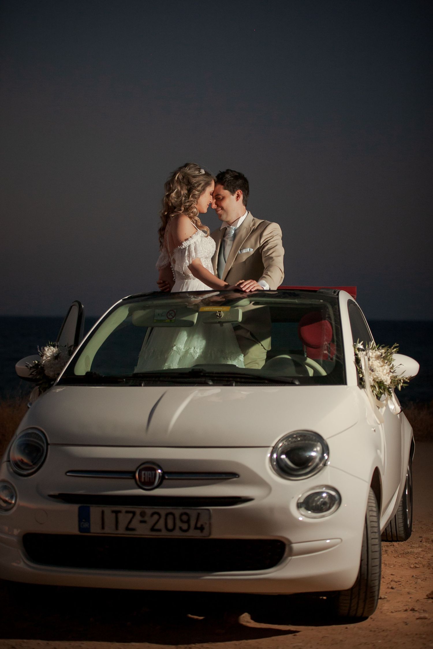 Romantic couple poses with white Fiat 500 car during sunset wedding photography session.
