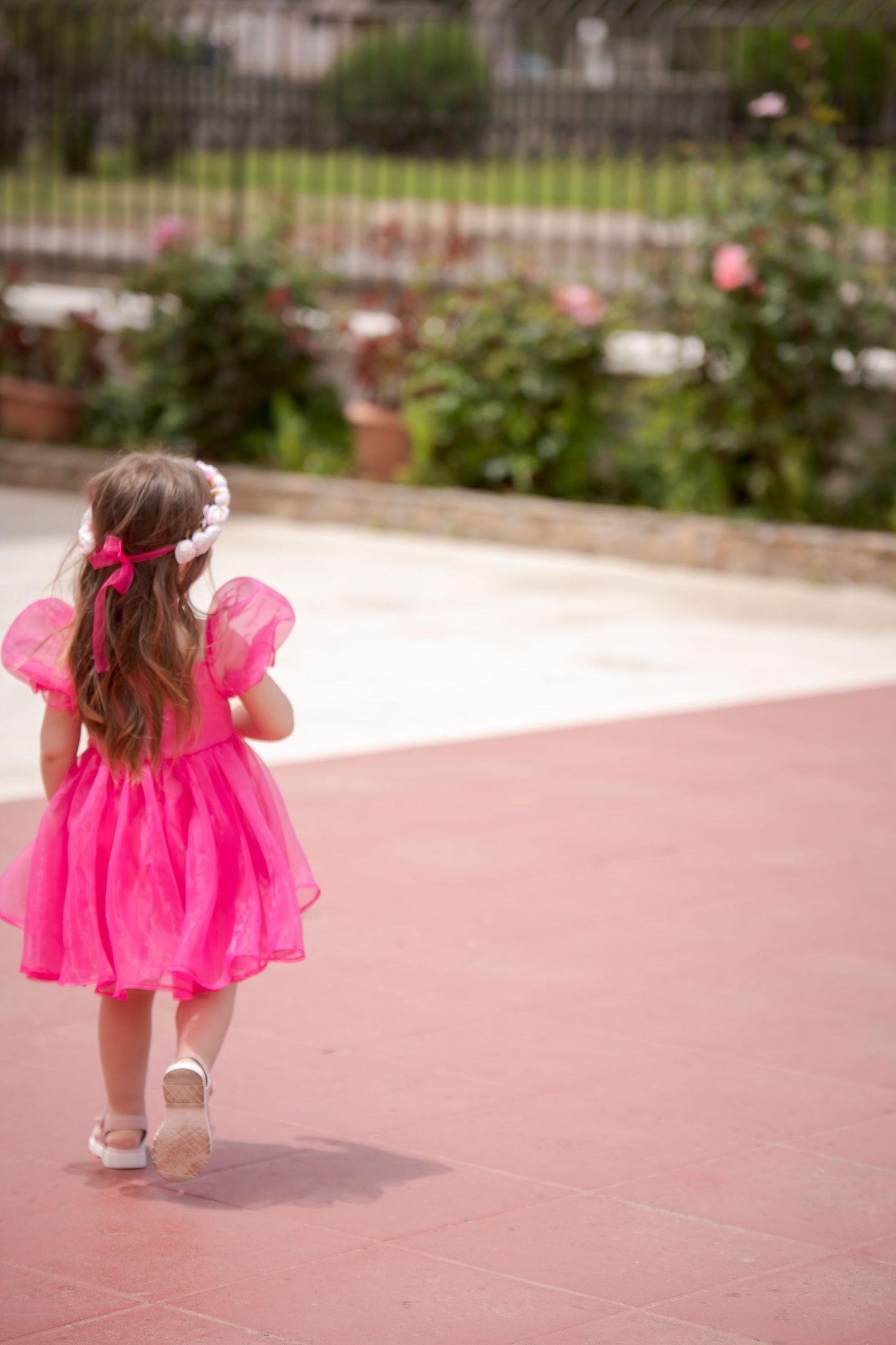 Child in bright pink tulle dress walking on concrete surface.
