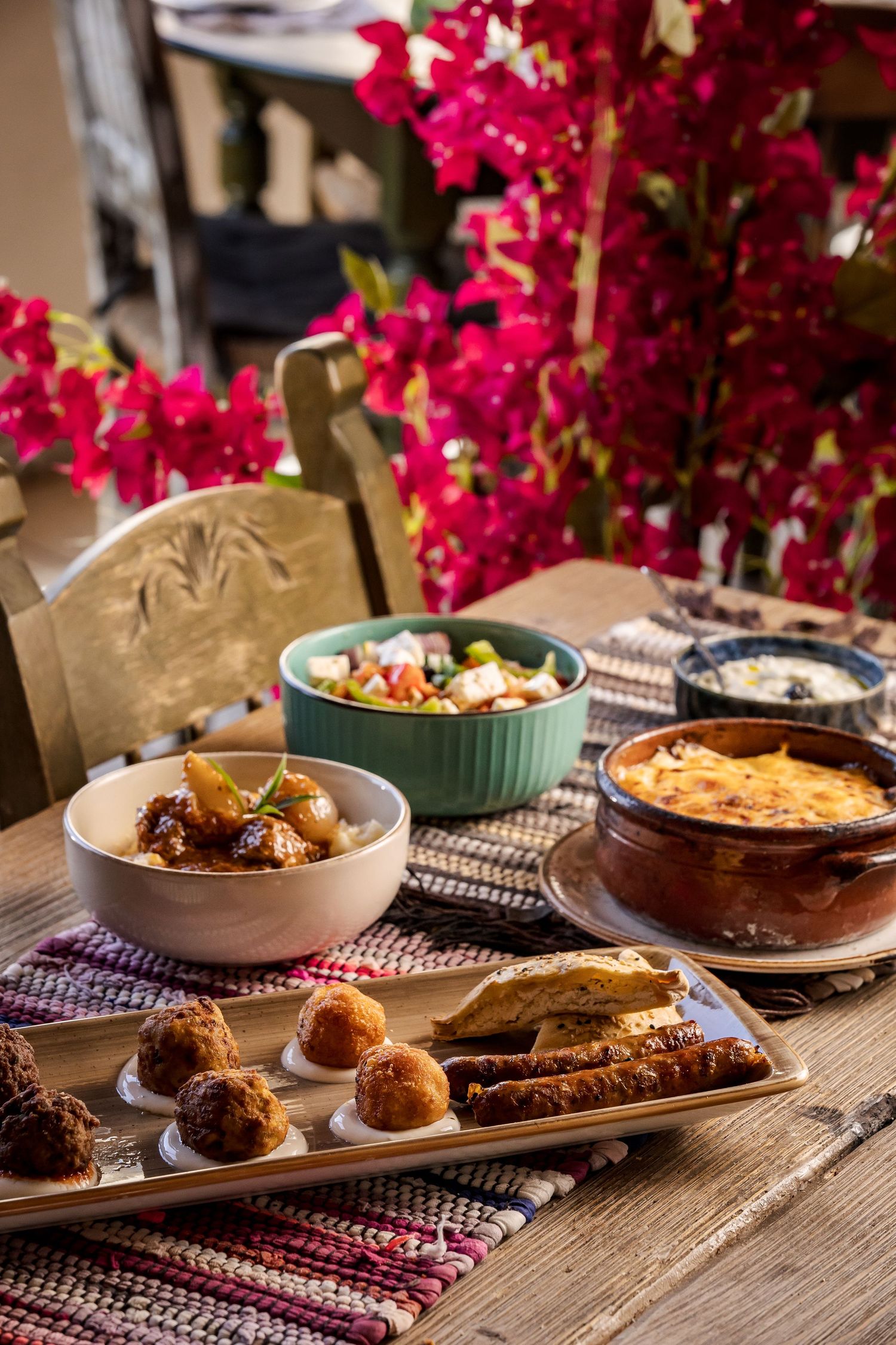 A rustic wooden table set with assorted chocolate desserts, baked goods, and bright pink flowers in elegant table settings.