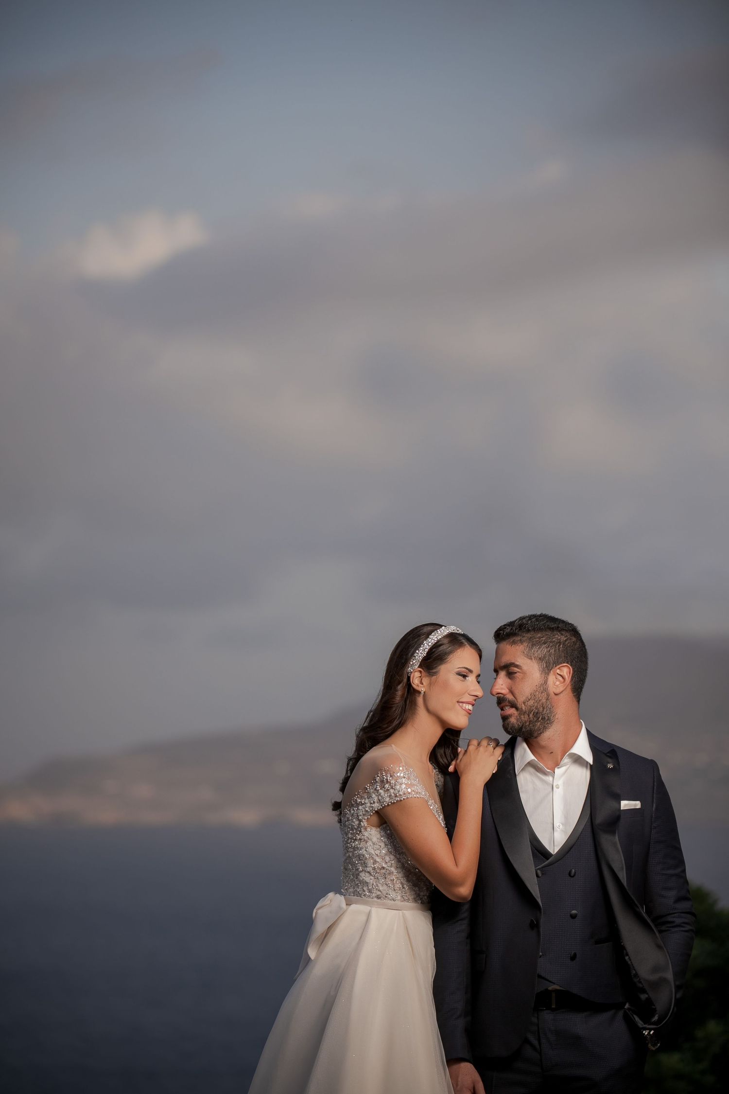Dramatic cloudy sky provides stunning backdrop for elegant wedding photography session.