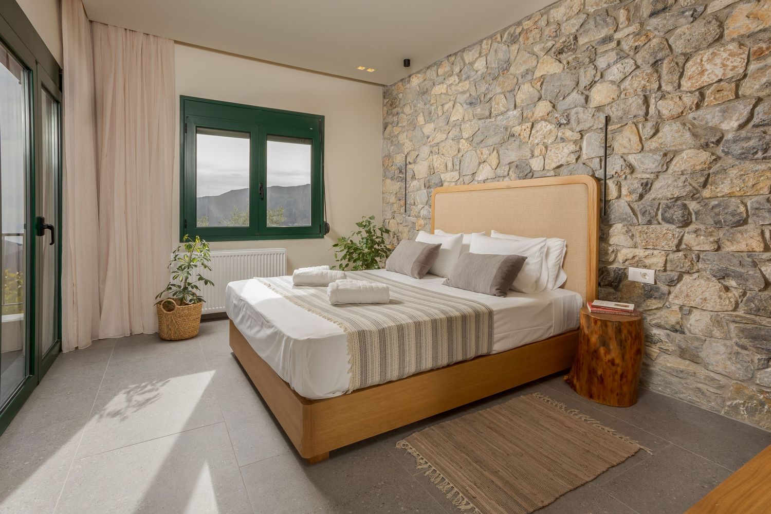 Modern bedroom features rustic stone walls, wooden flooring, and minimalist decor with natural light streaming in.