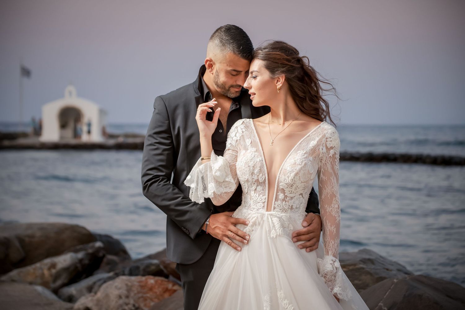 Elegant coastal wedding portraits with bride in lace dress near ocean.