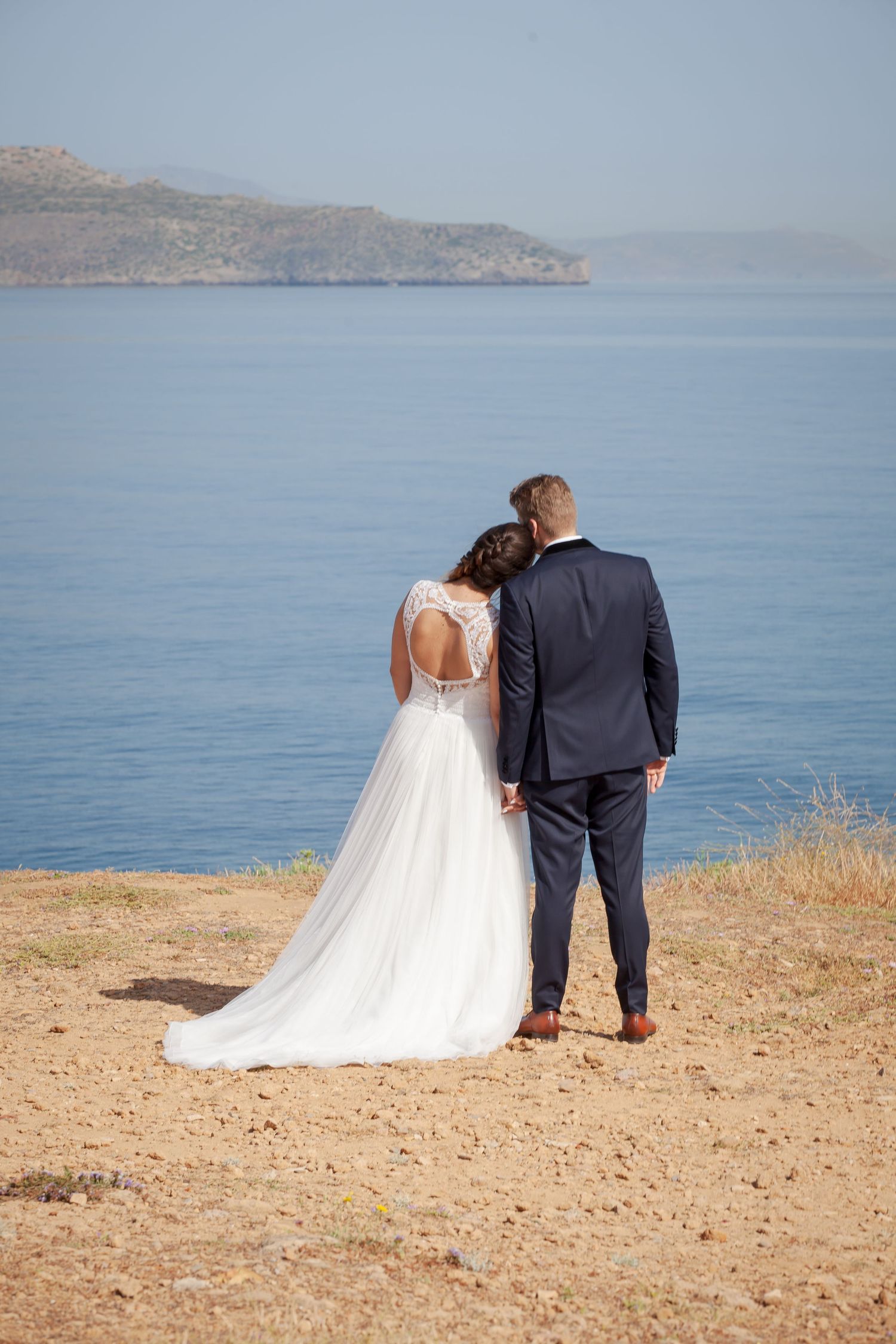 Couple overlooks serene ocean vista in elegant wedding attire.