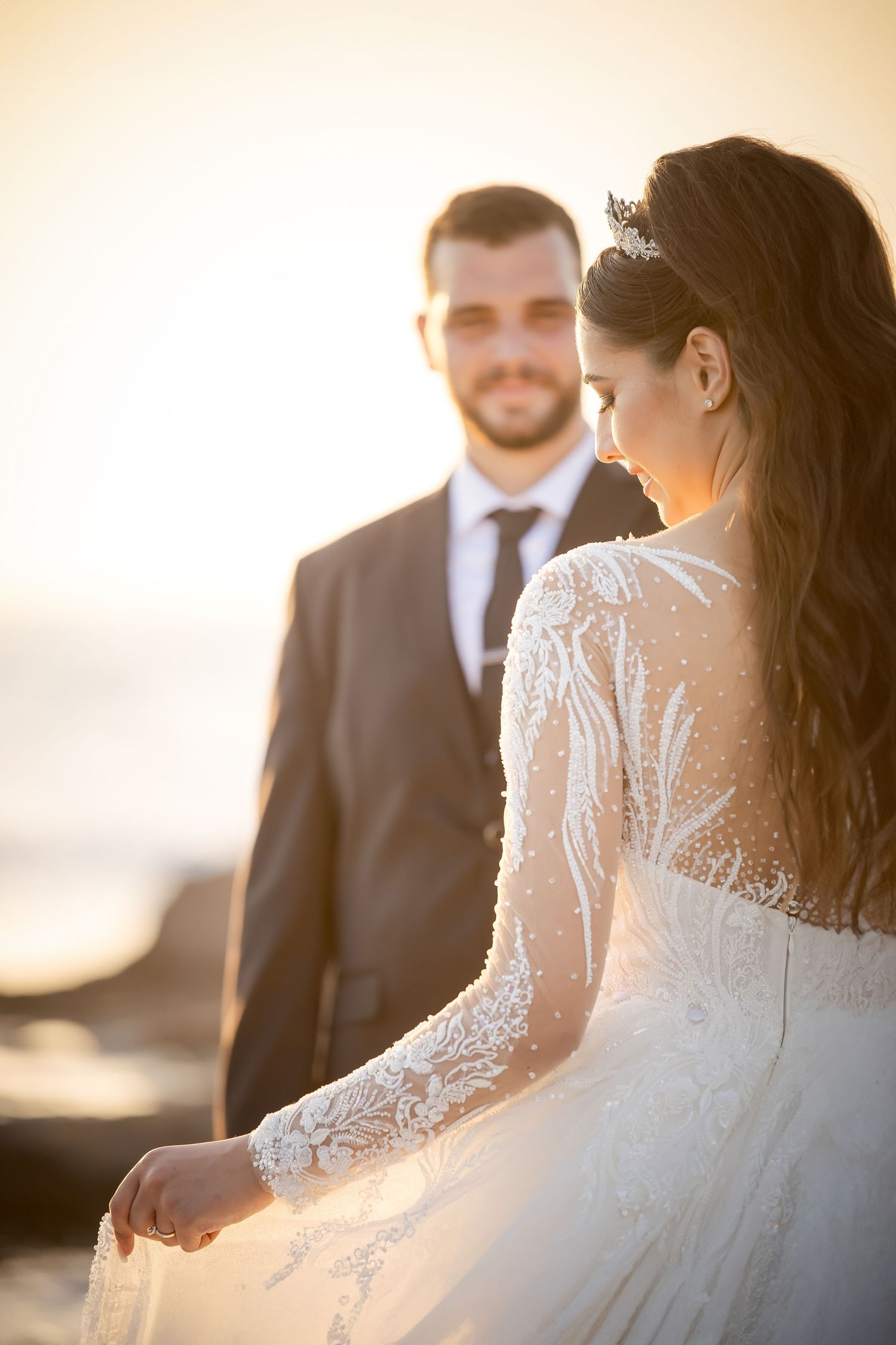 Elegant wedding couple stands in soft golden light showcasing details of lace gown.