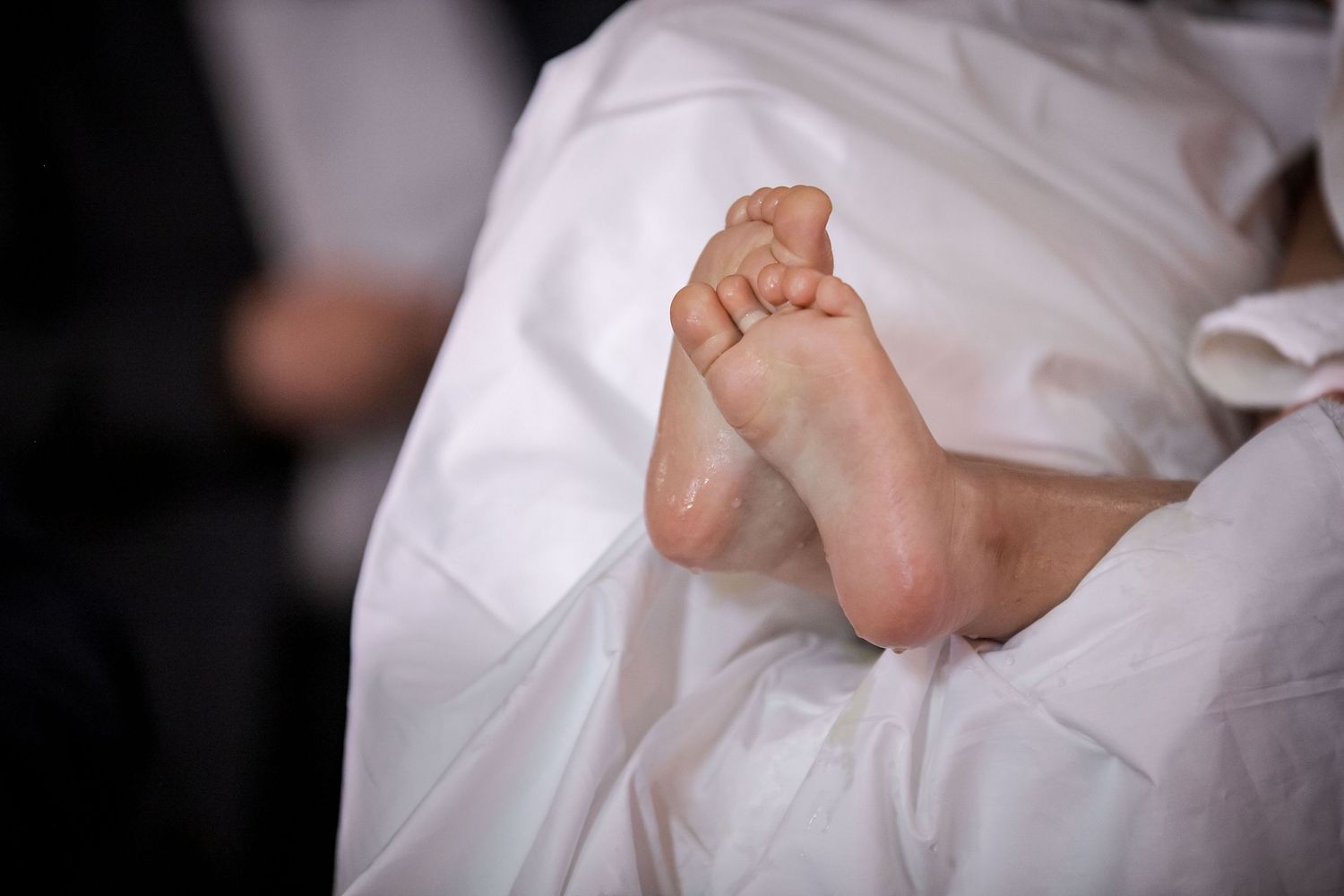 Bare feet peeking out from under white fabric in dramatic lighting.