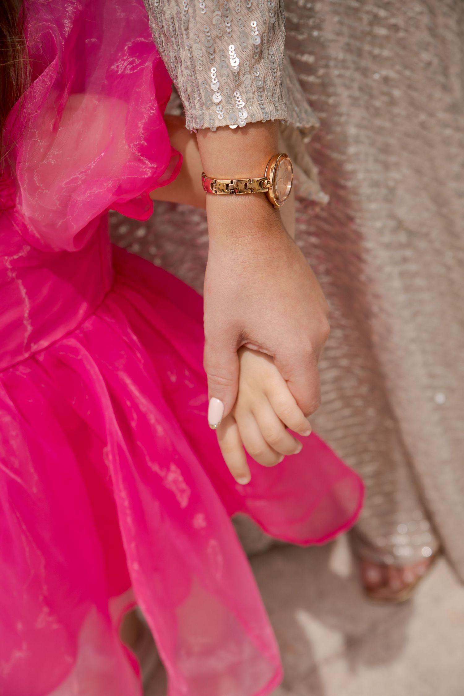 Hands holding delicate fabric of a bright pink dress against a sparkly silver background.
