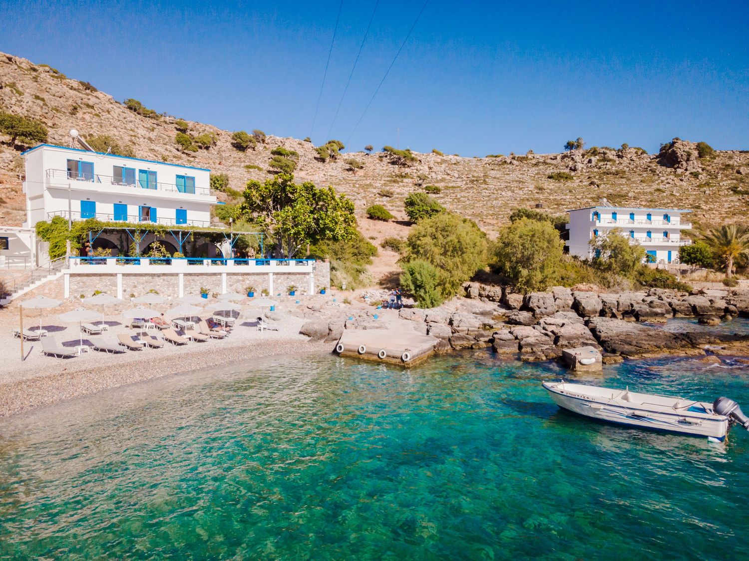 Panoramic view of turquoise bay with white buildings along rocky Mediterranean coastline.