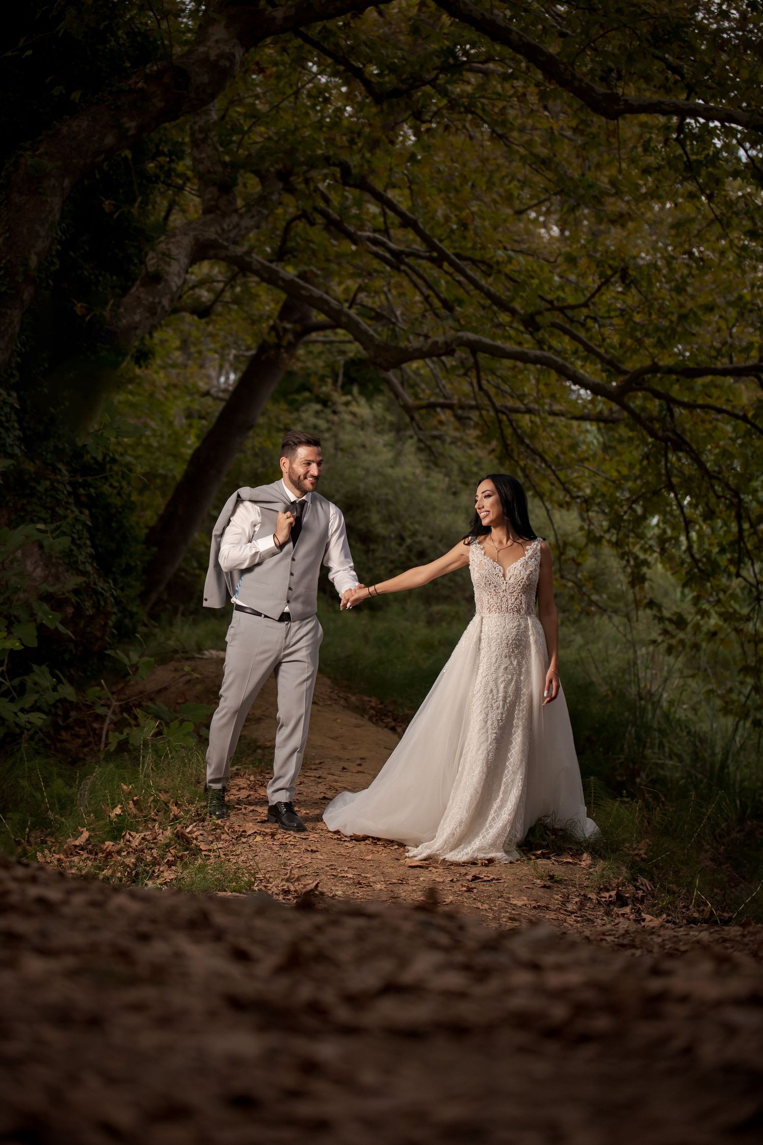 Forest wedding photo session with couple dancing among autumn leaves and tree shadows.