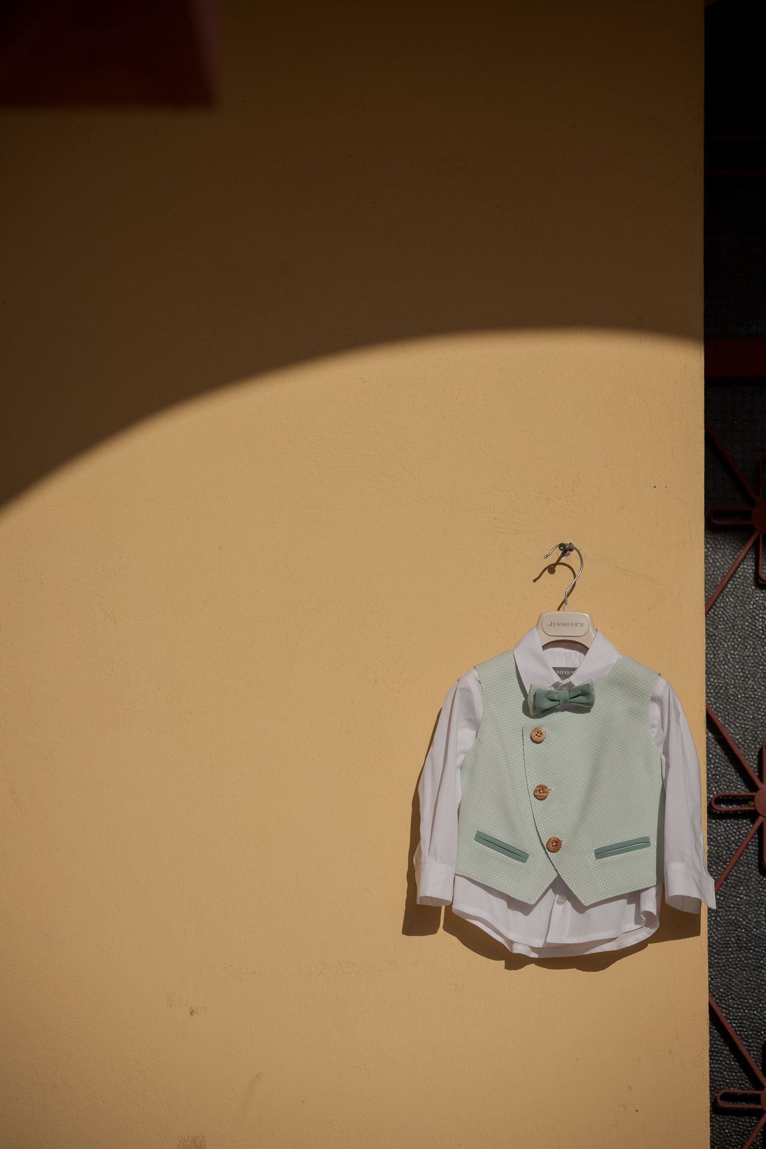 White formal vest or jacket hanging against a beige wall in dramatic lighting.