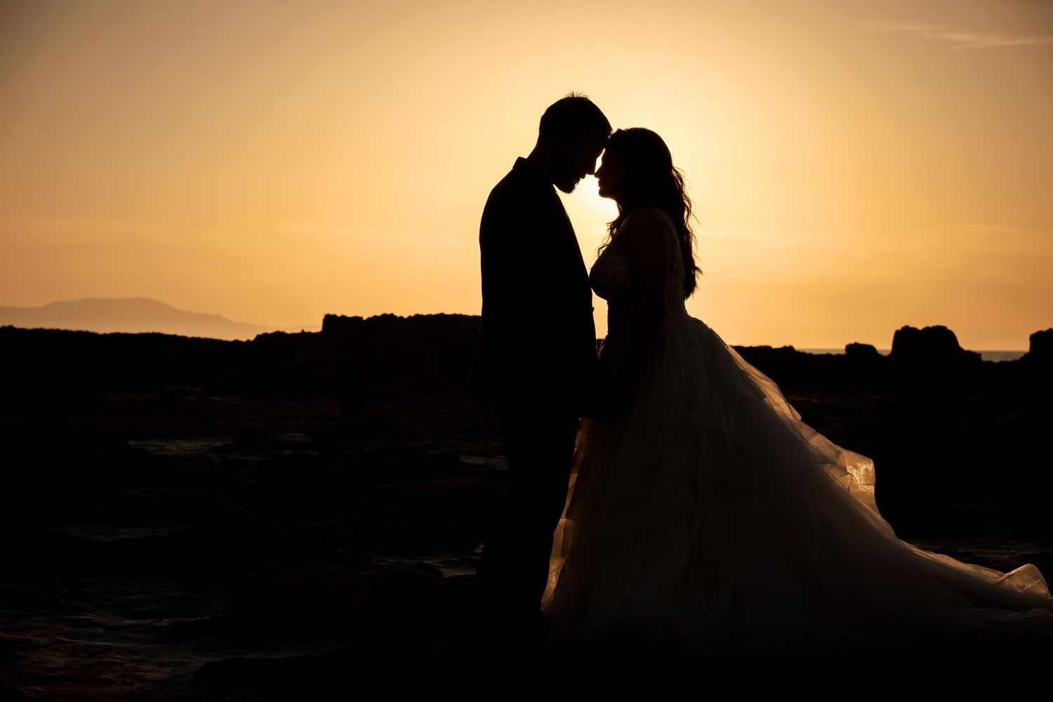 Silhouettes against majestic sunset backdrop during coastal wedding photography session.