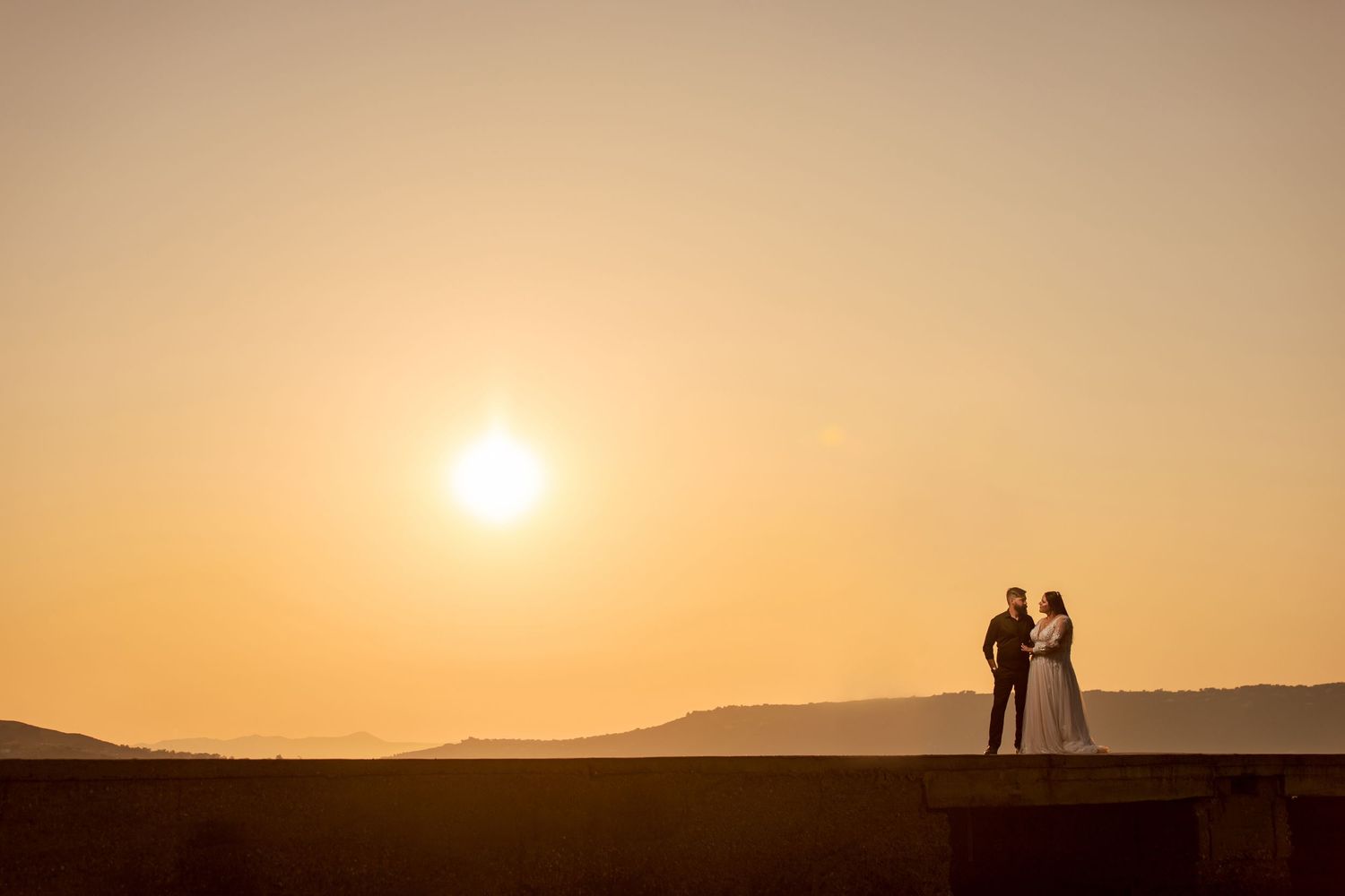 Romantic sunset silhouette against desert landscape with mountains in background.