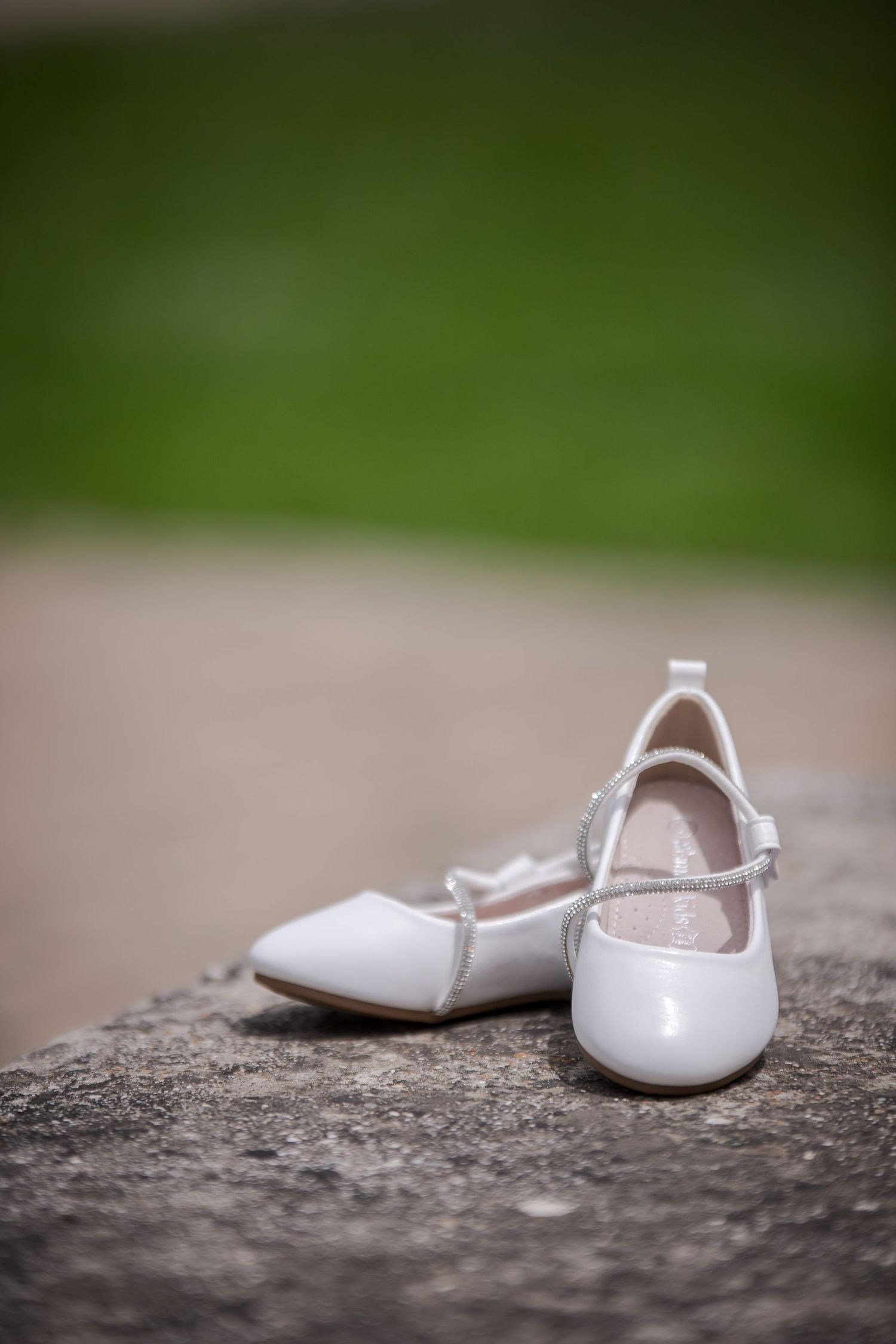White patent leather children's dress shoes arranged on stone surface.