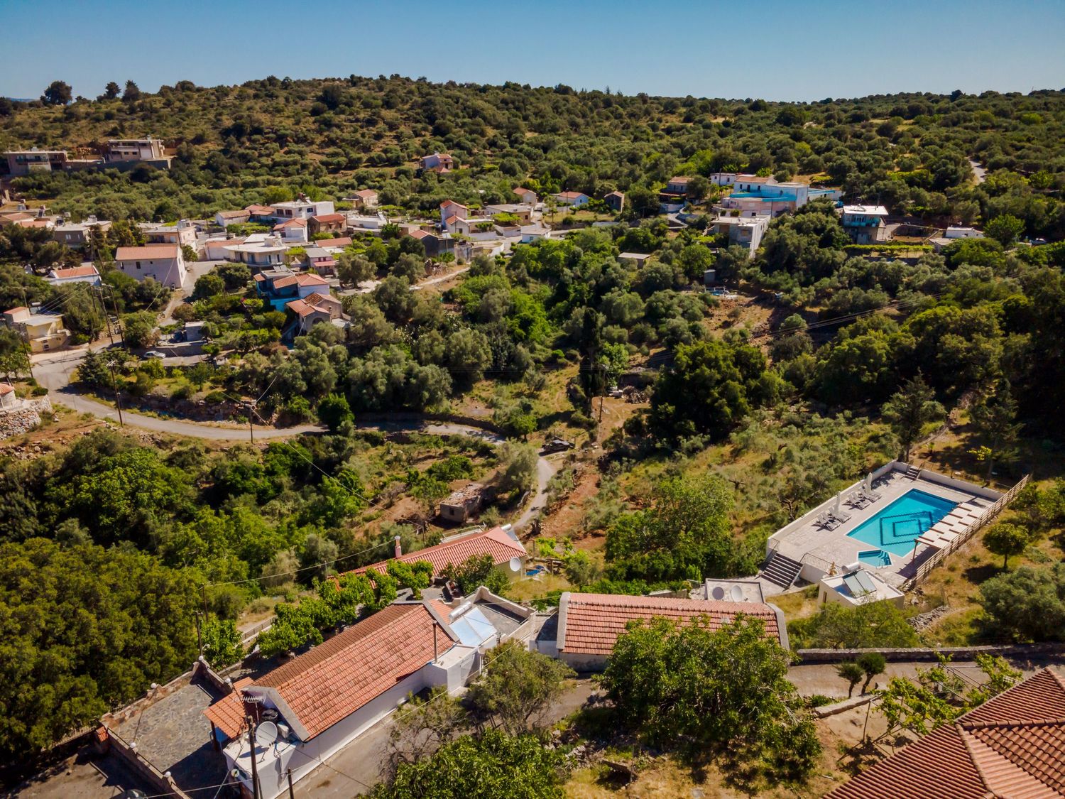 Aerial view of Mediterranean coastal villas and swimming pools nestled in hillside terrain.