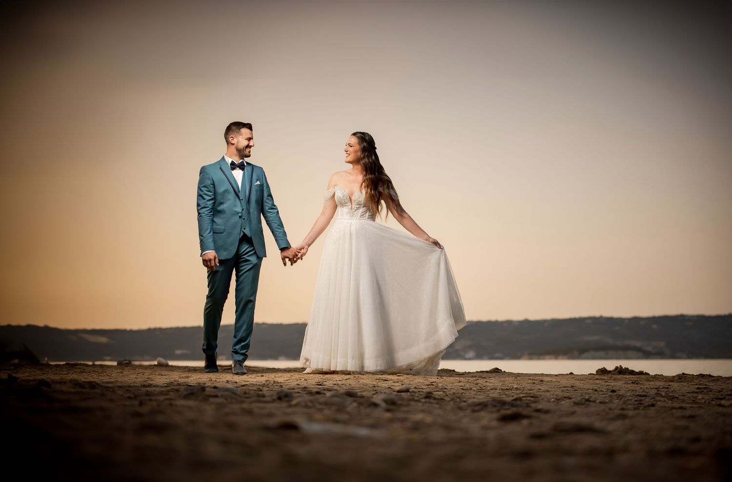 Wedding couple walks along sandy beach during sunset photo session.