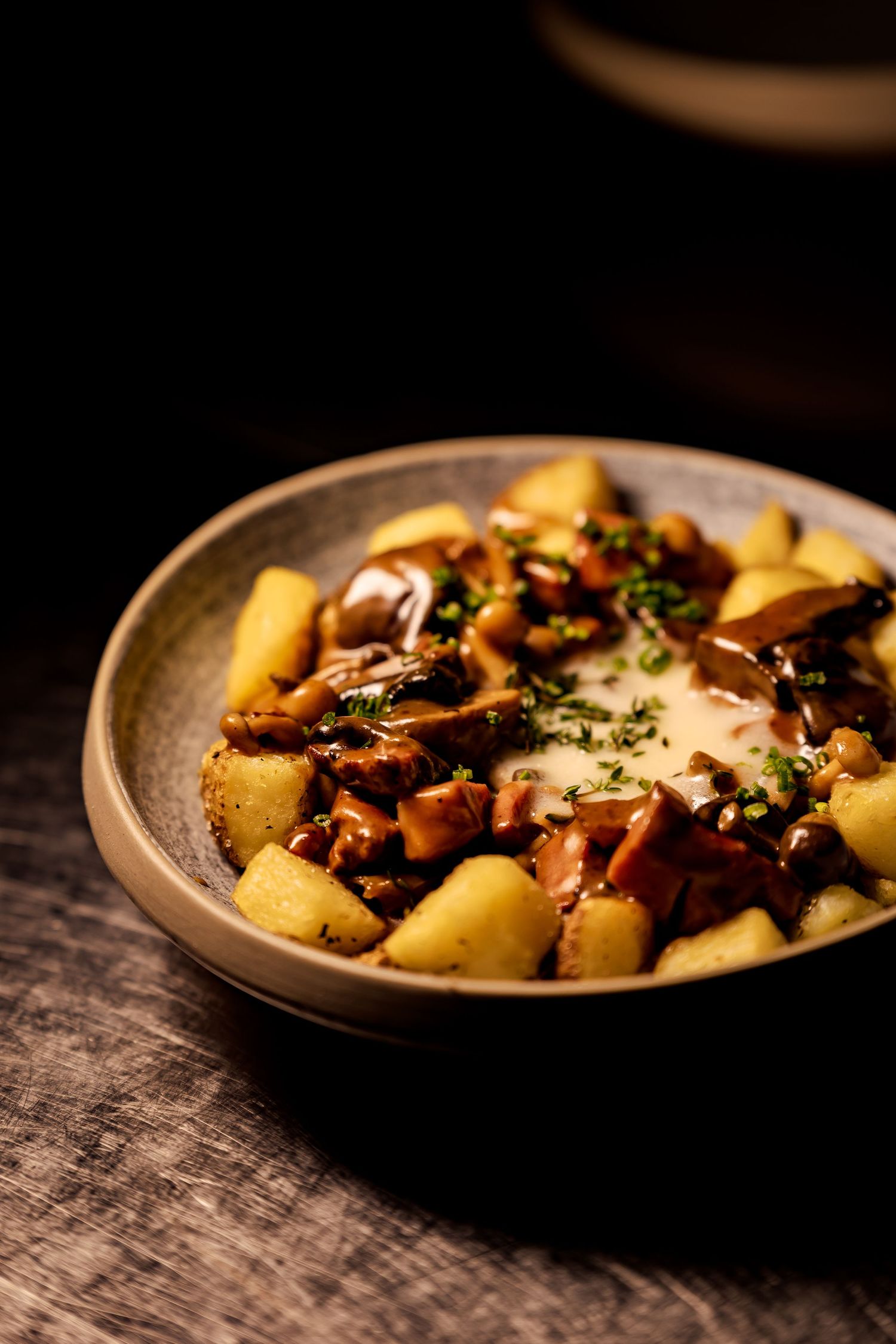 Rustic serving of roasted potatoes with mushrooms and herbs on a dark ceramic plate against a textured wooden surface.